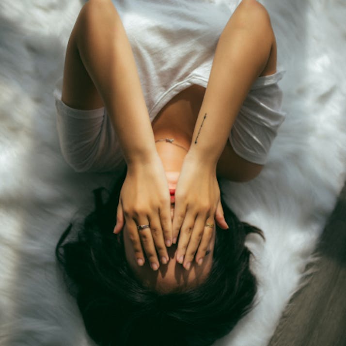 Woman laying down covering her face with her hands.