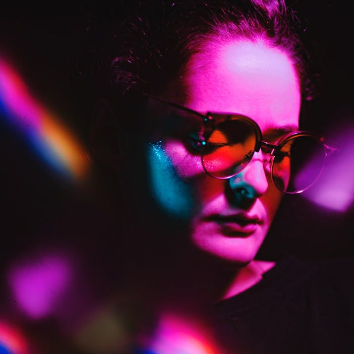 A woman wearing glasses, illuminated with a pink light.