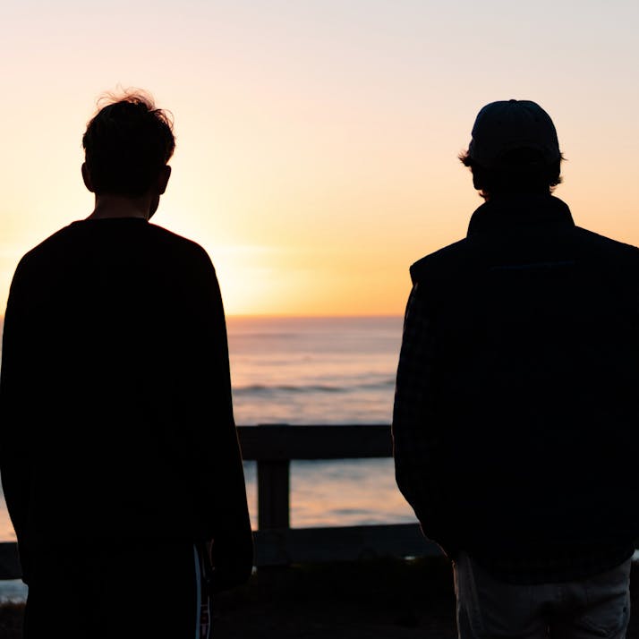 Two people's silhouettes, staring out at the sunset over an ocean.