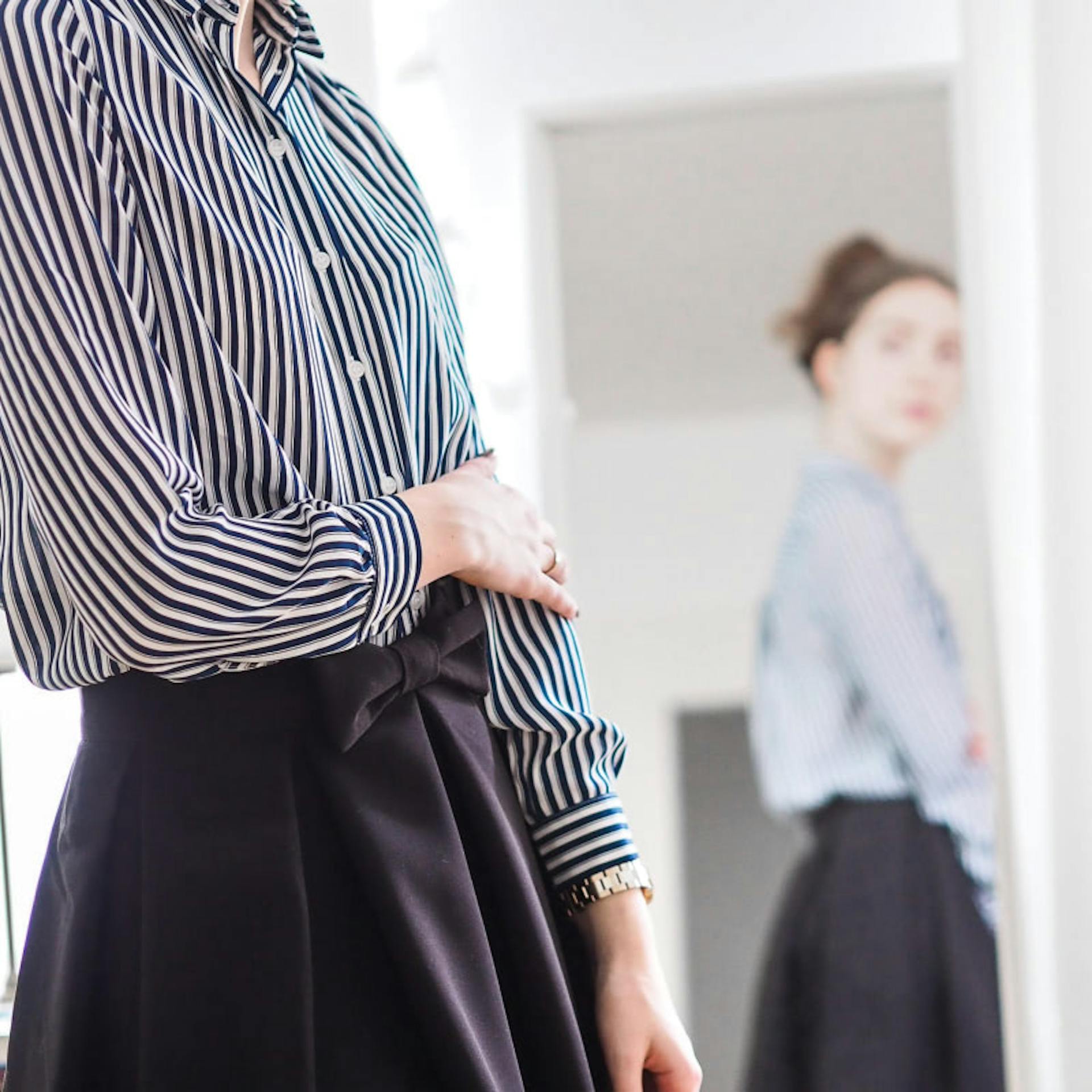 A woman self-consciously observes her outfit in the mirror.
