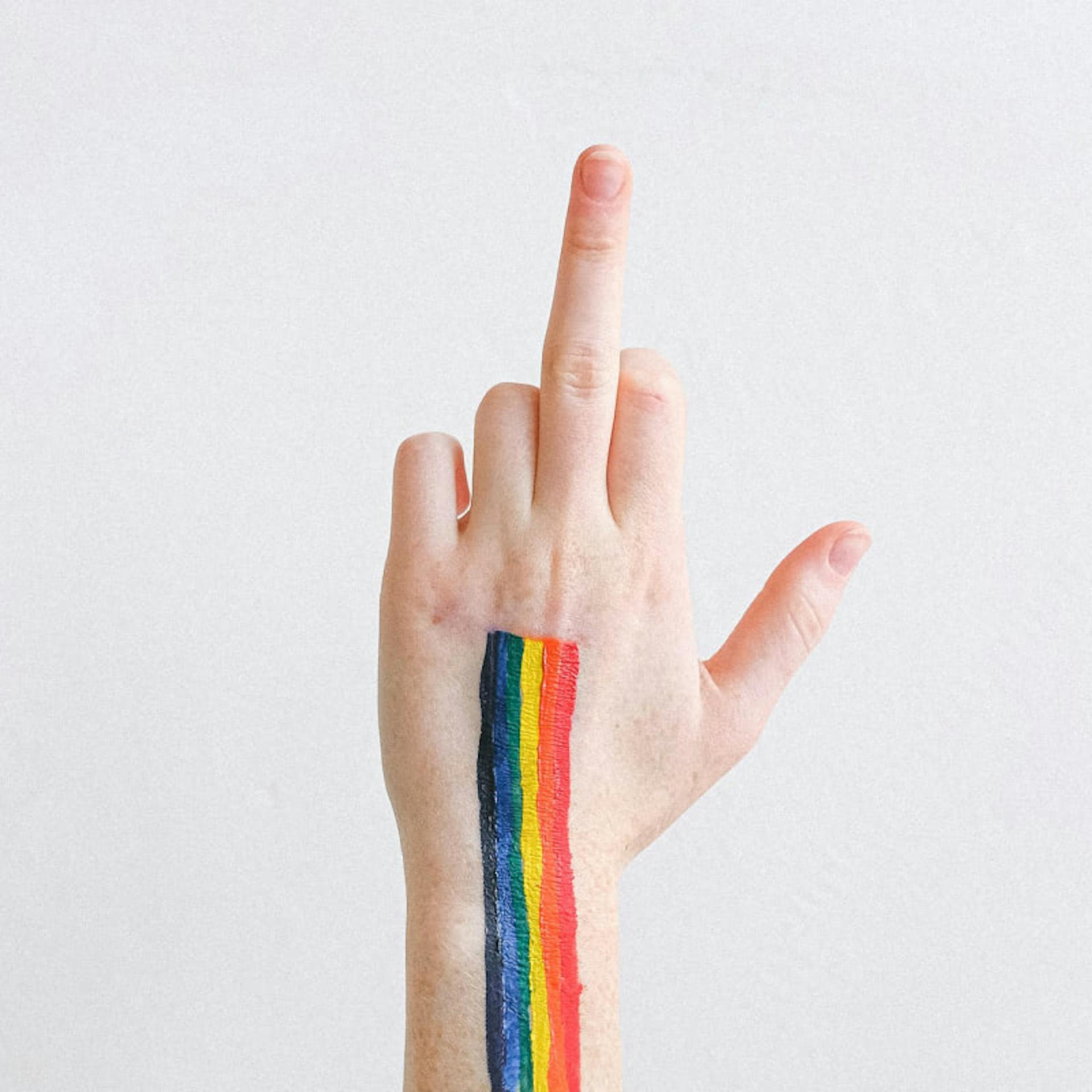 A raised middle finger with a rainbow flag painted on the hand.