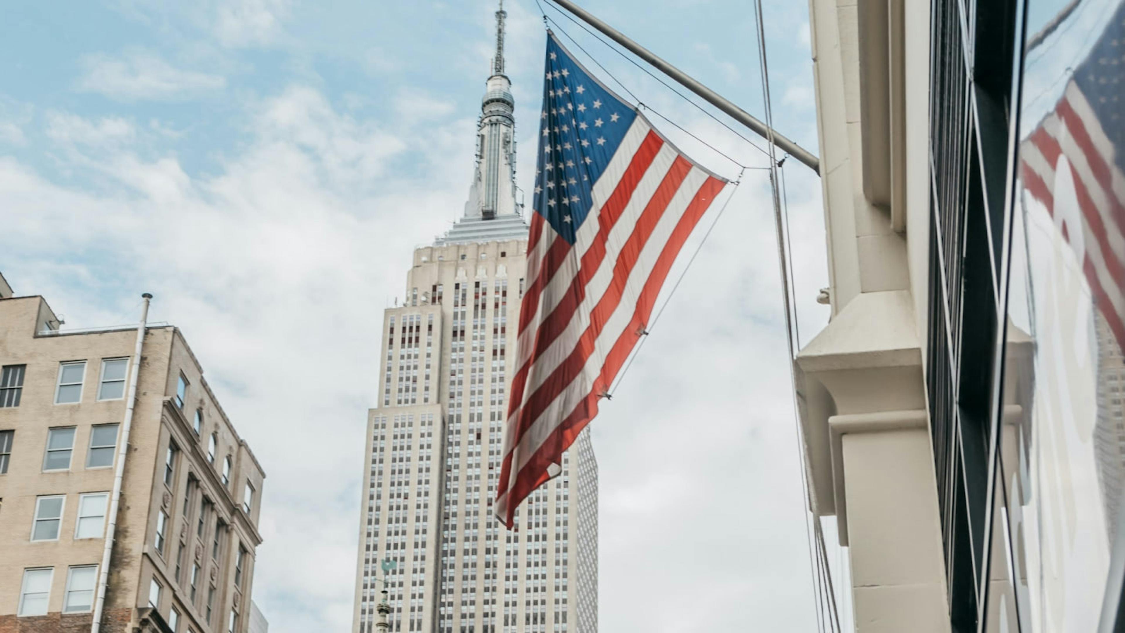 An American flag with the Empire State Building in New York in the background.