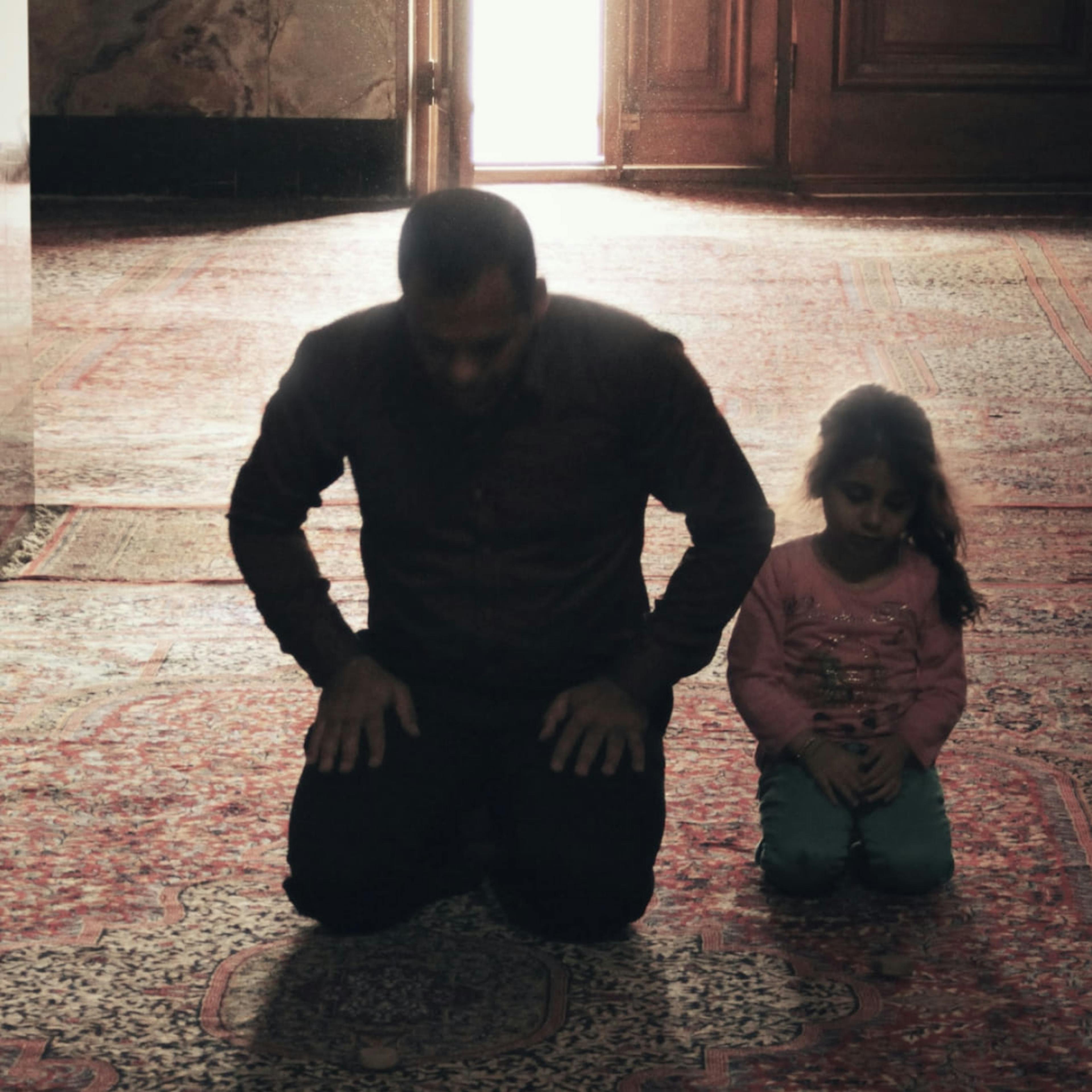A young Pakistani-American girl prays with her father at mosque.