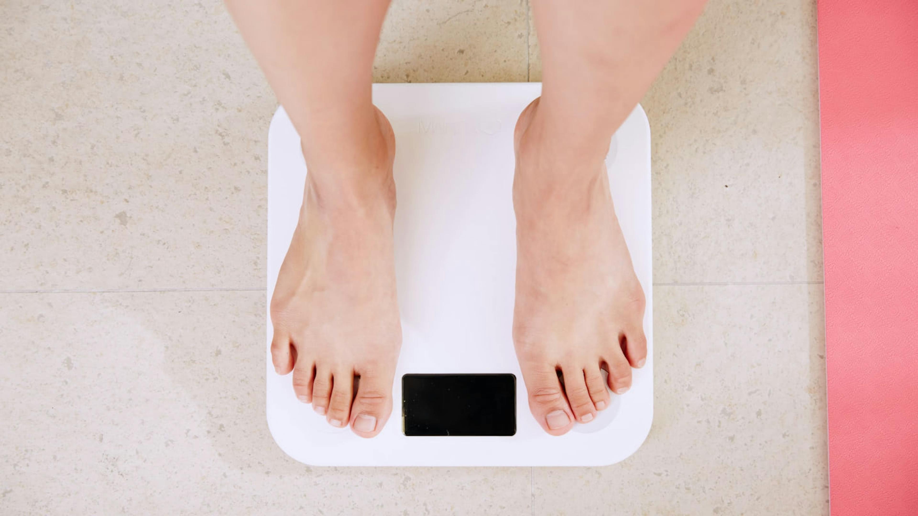 A person who struggles with their weight stands on a scale.