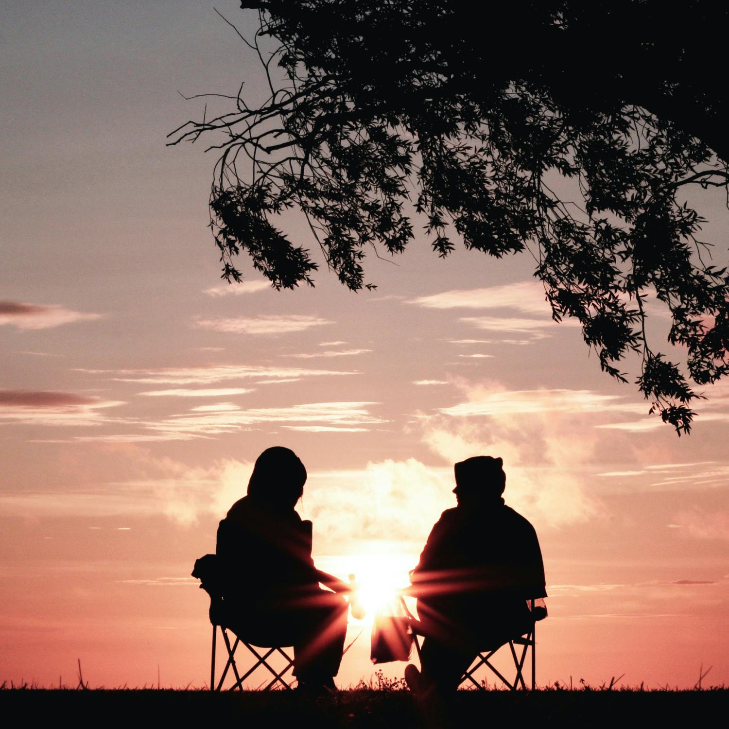 A silhouette of two people seated outside, under a tree.