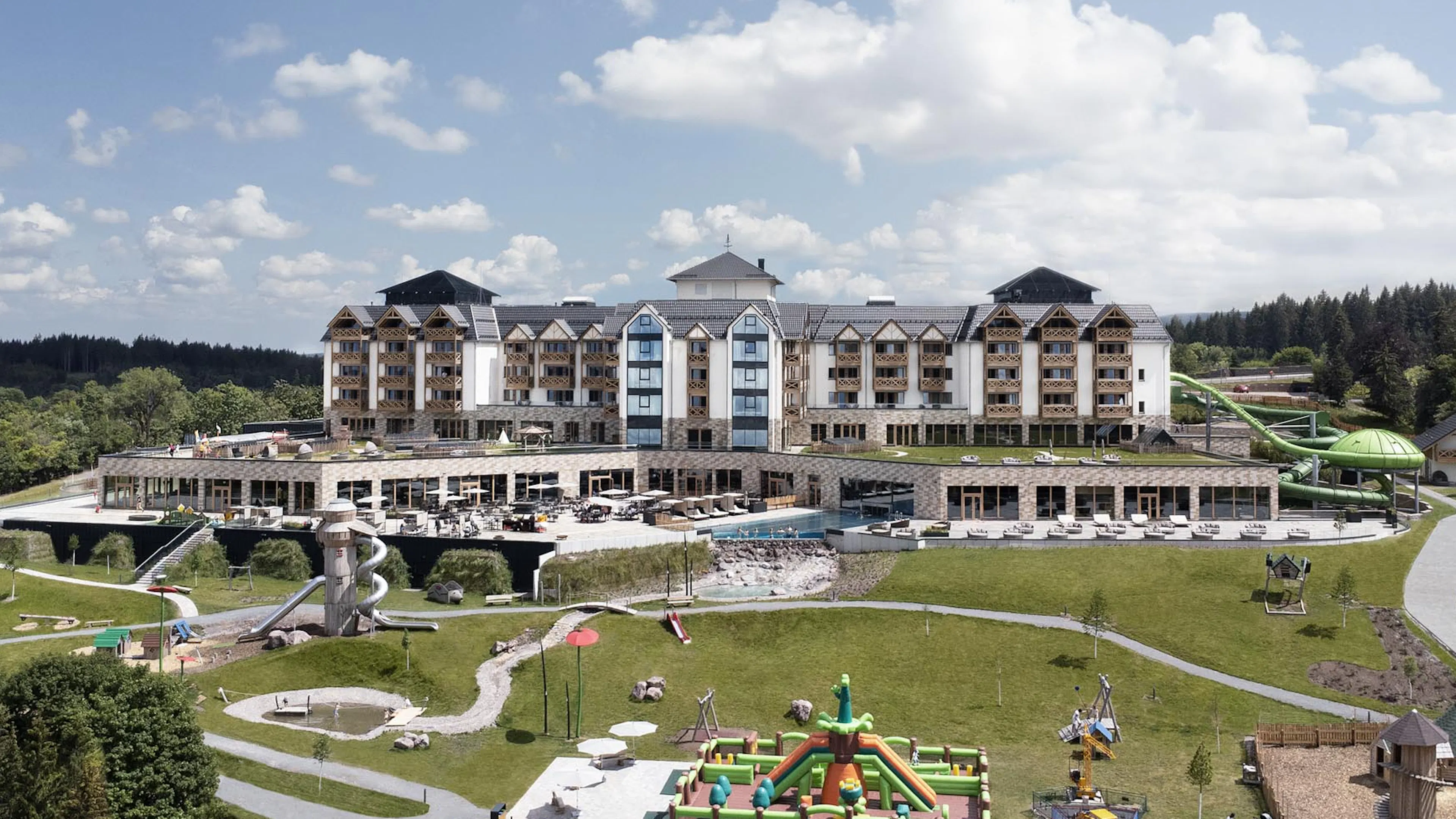 Sommerliche Hotelansicht des The Grand Green - Familux Resorts mit Spielplatz.