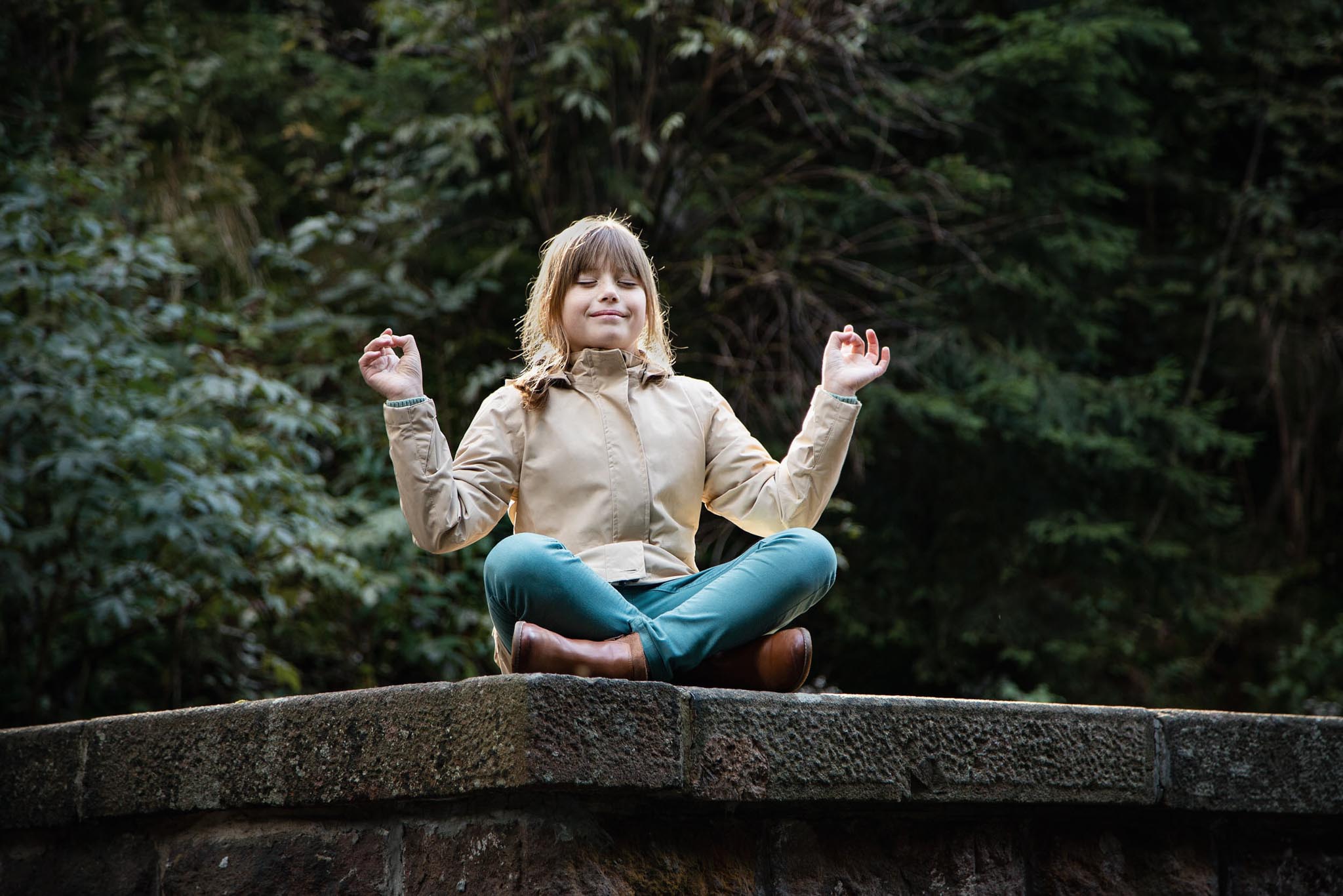 Girl sitting on a wall in a forest in autumn in a yoga pose.