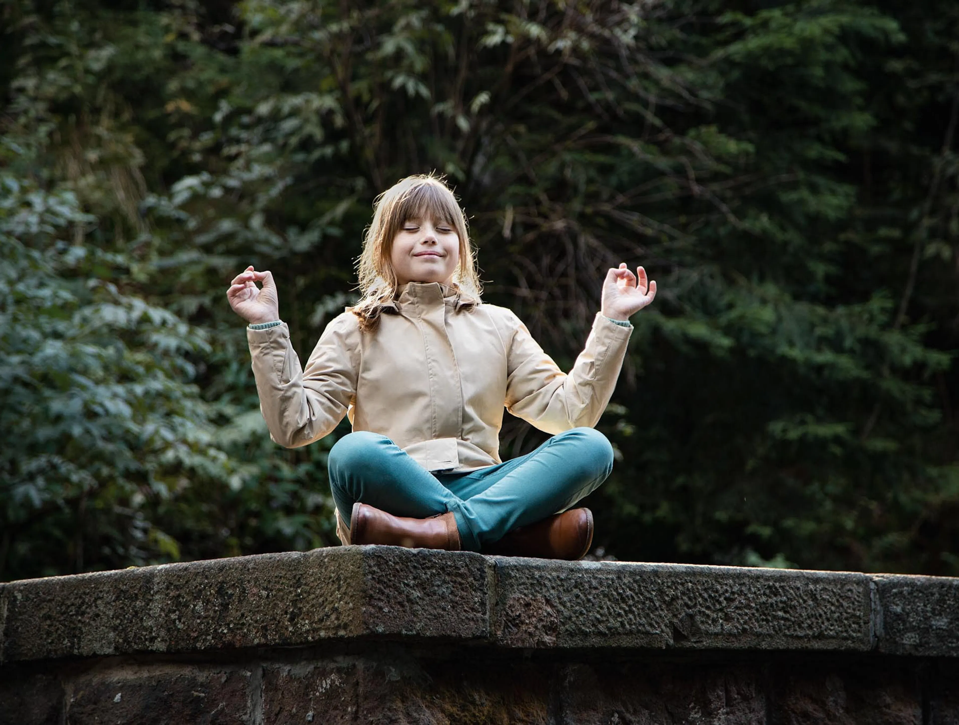 Girl sitting on a wall in a forest in autumn in a yoga pose.