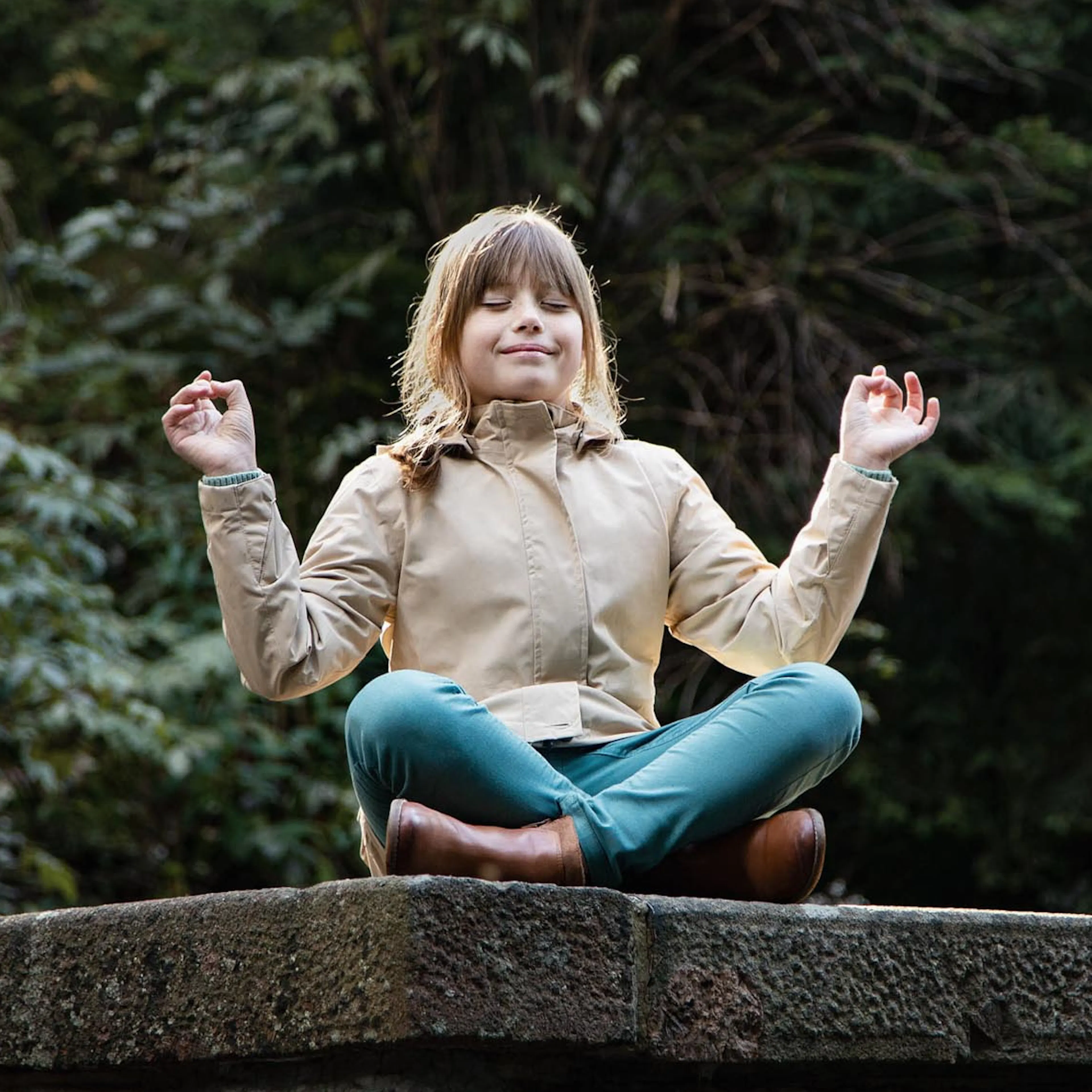 Girl sitting on a wall in a forest in autumn in a yoga pose.