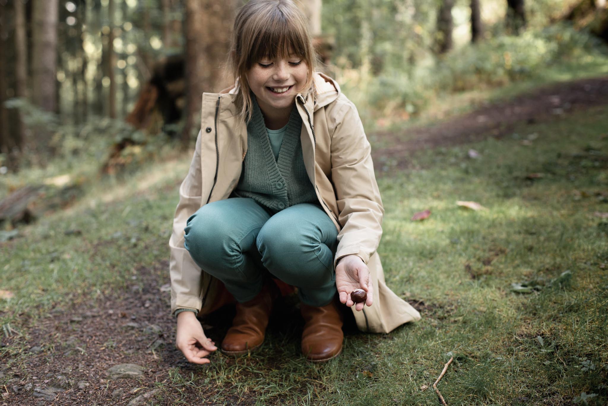 Girl picking up a chestnut in the forest.