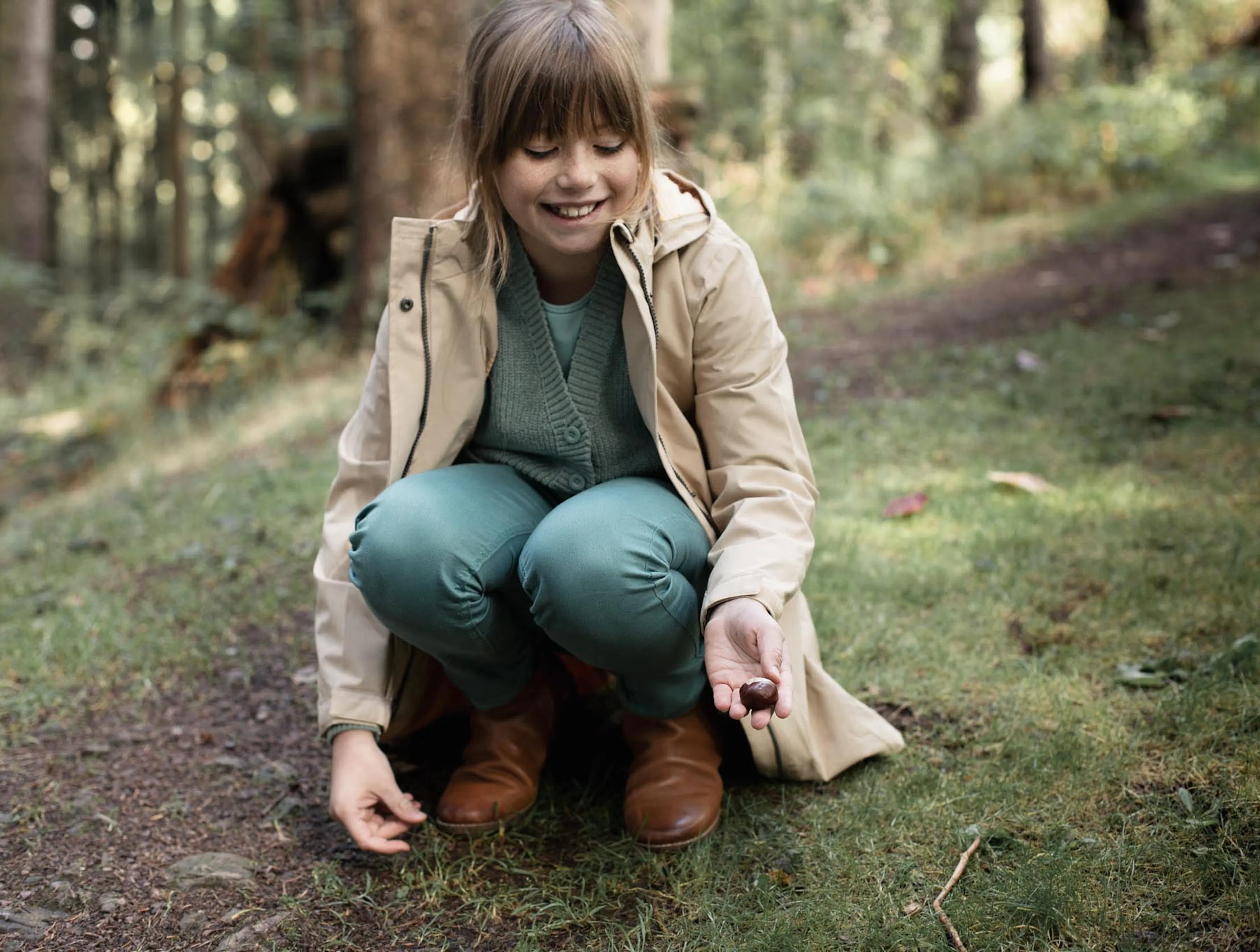 Girl picking up a chestnut in the forest.