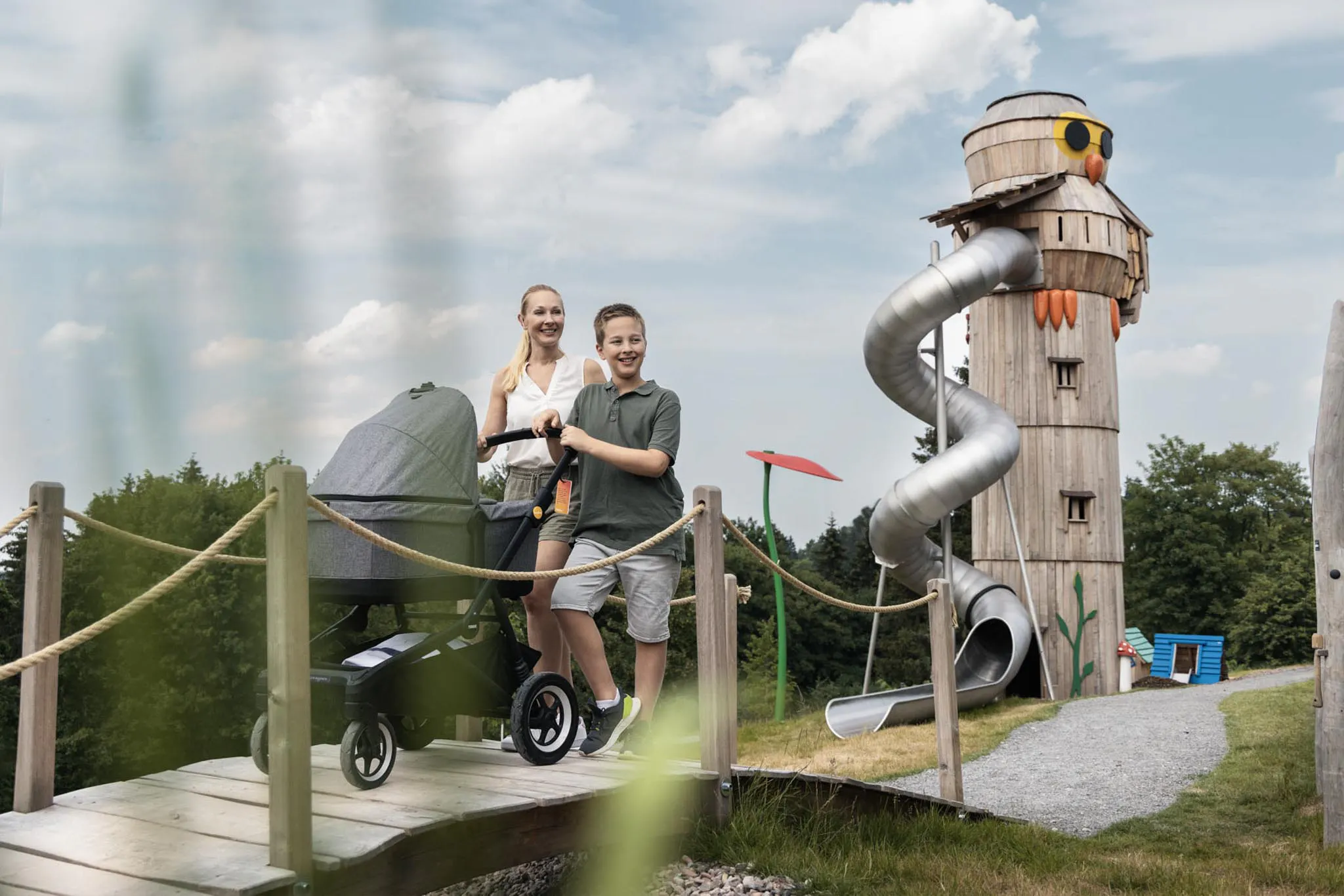 Mama und Sohn spazieren mit Kinderwagen durch den Hotelgarten des The Grand Green - Familux Resorts.