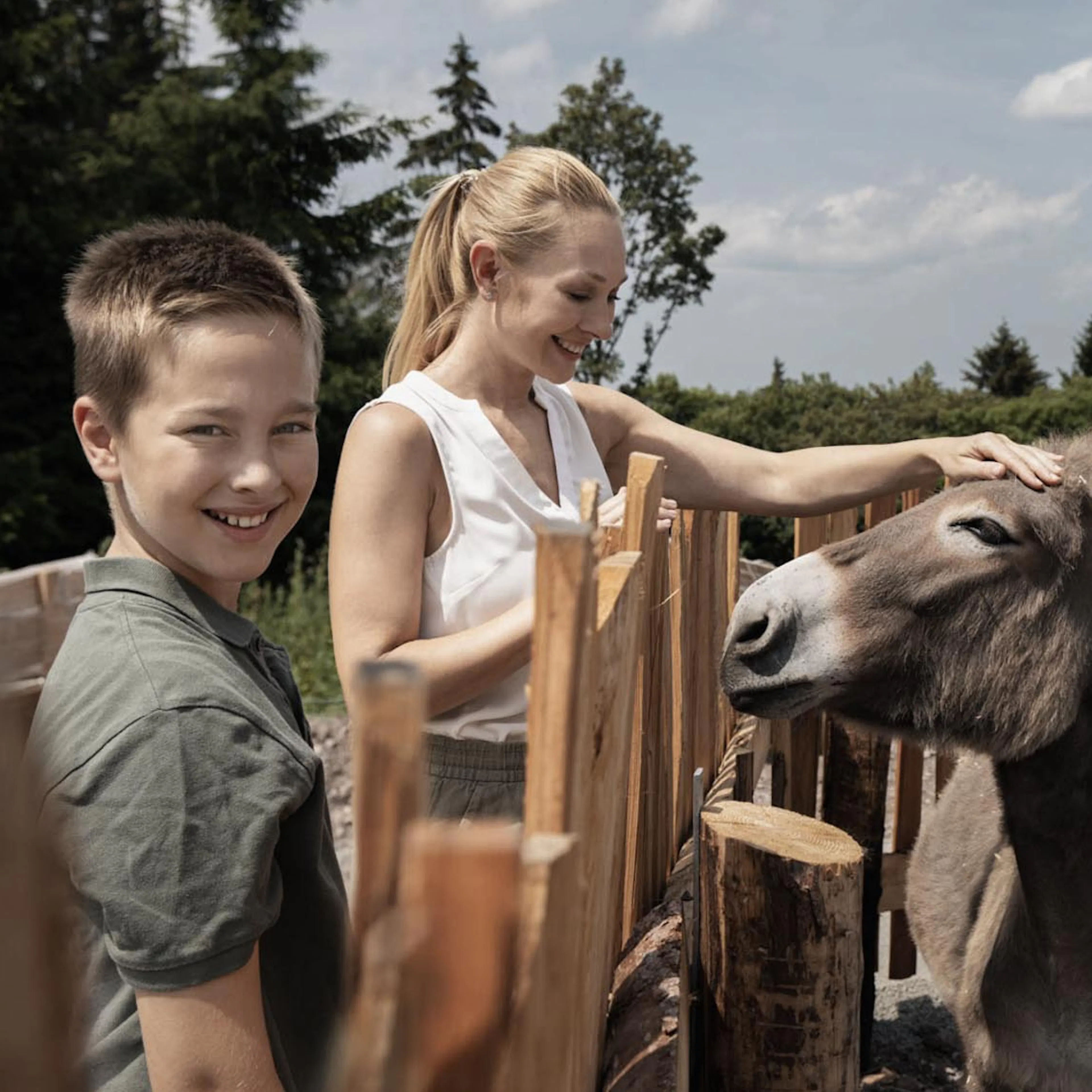 Mama und Sohn streicheln einen Esel aus dem Streichelzoo des The Grand Green - Familux Resorts.