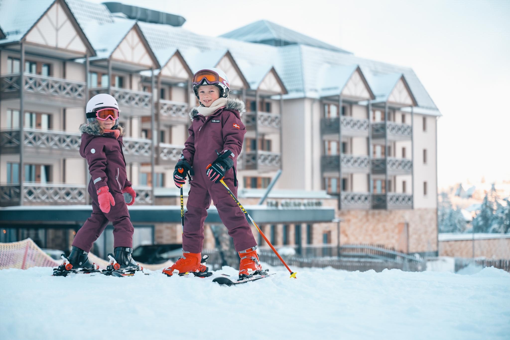 Zwei Mädchen im Skioutfit beim Skikurs vor dem The Grand Green - Familux Resort.