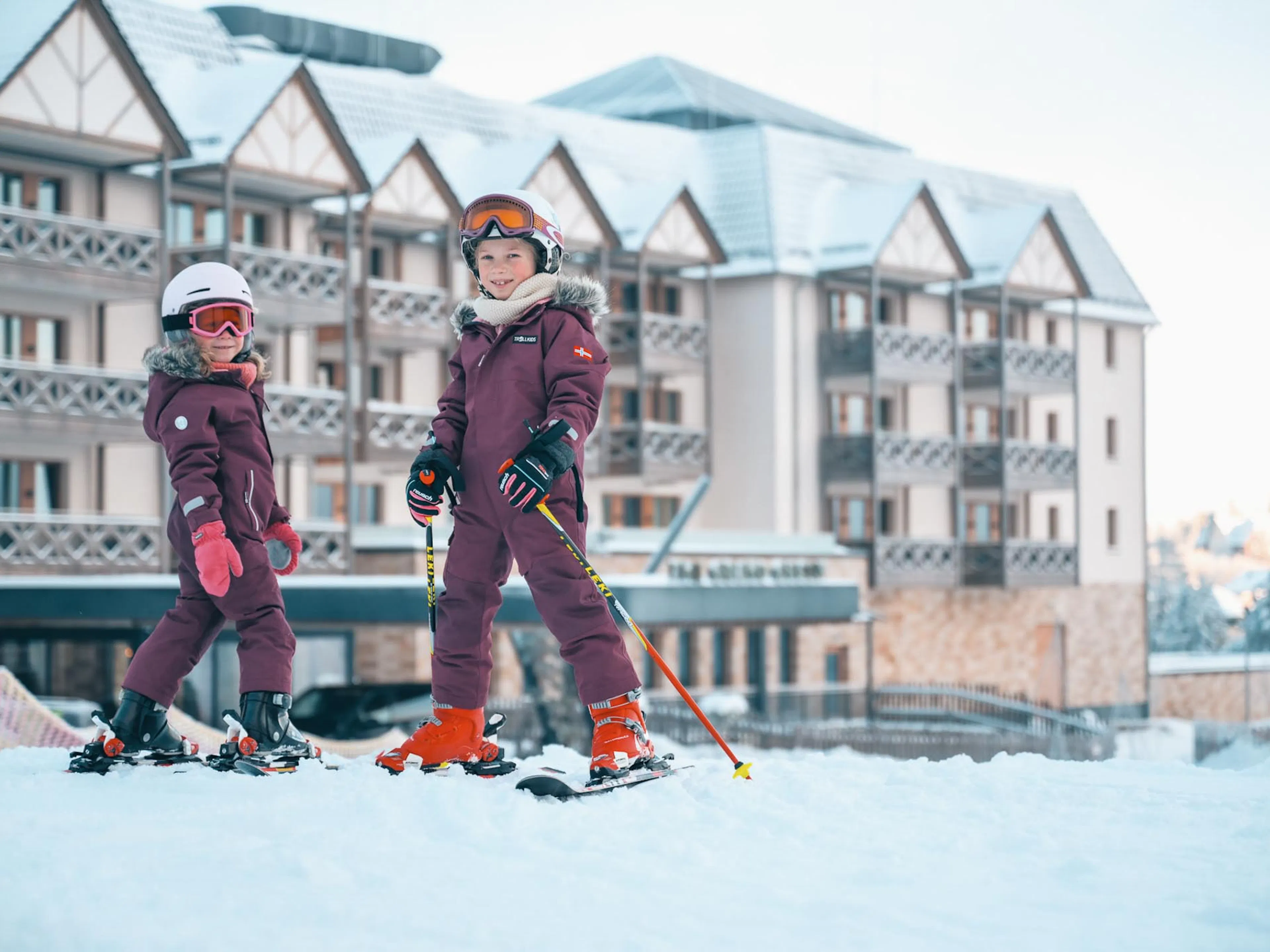Zwei Mädchen im Skioutfit beim Skikurs vor dem The Grand Green - Familux Resort.