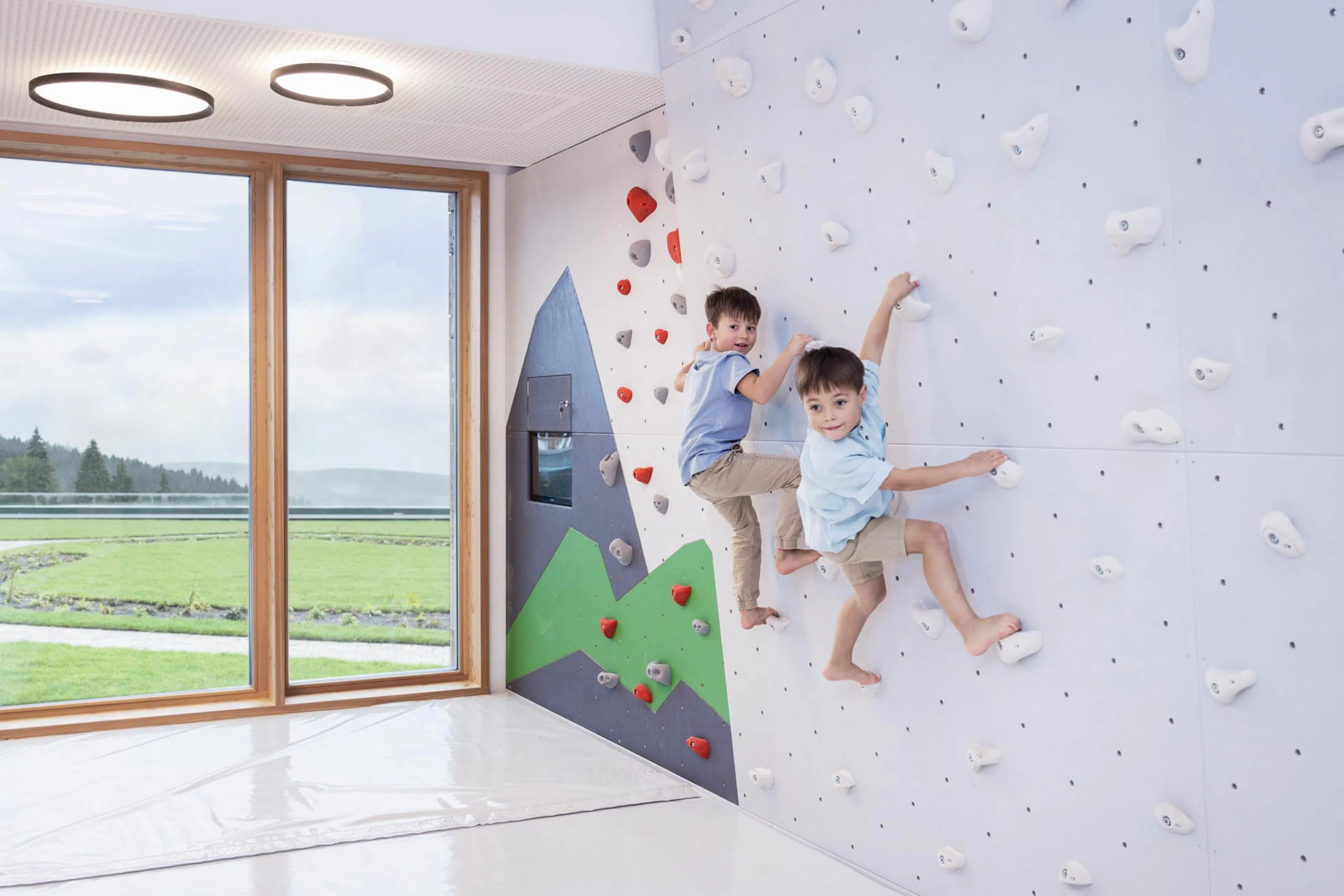 Two boys climbing on the climbing wall in the Kids Club at The Grand Green – Familux Resort.