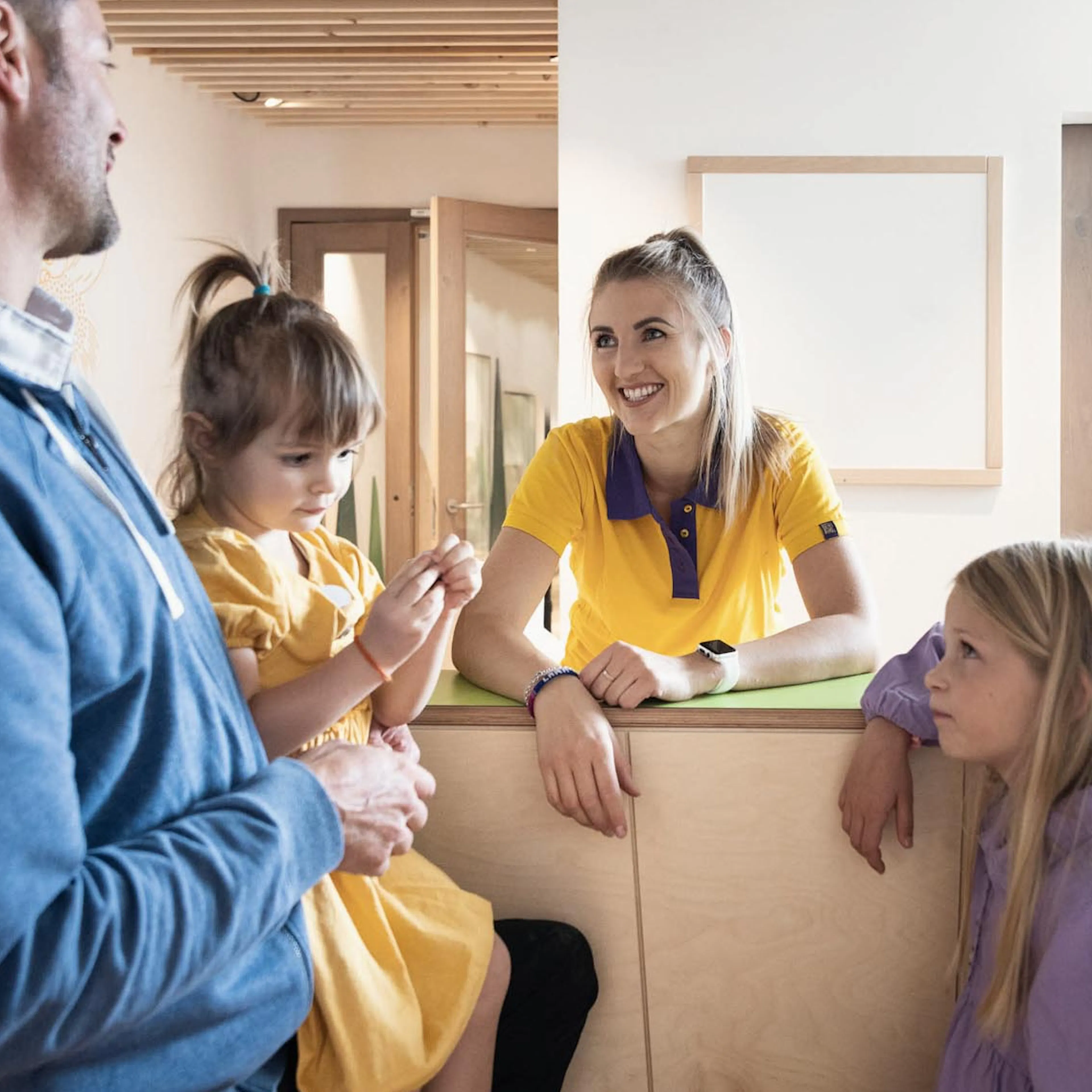 Father registering his children at the Kids Club reception desk with the childcare team at The Grand Green – Familux Resort.