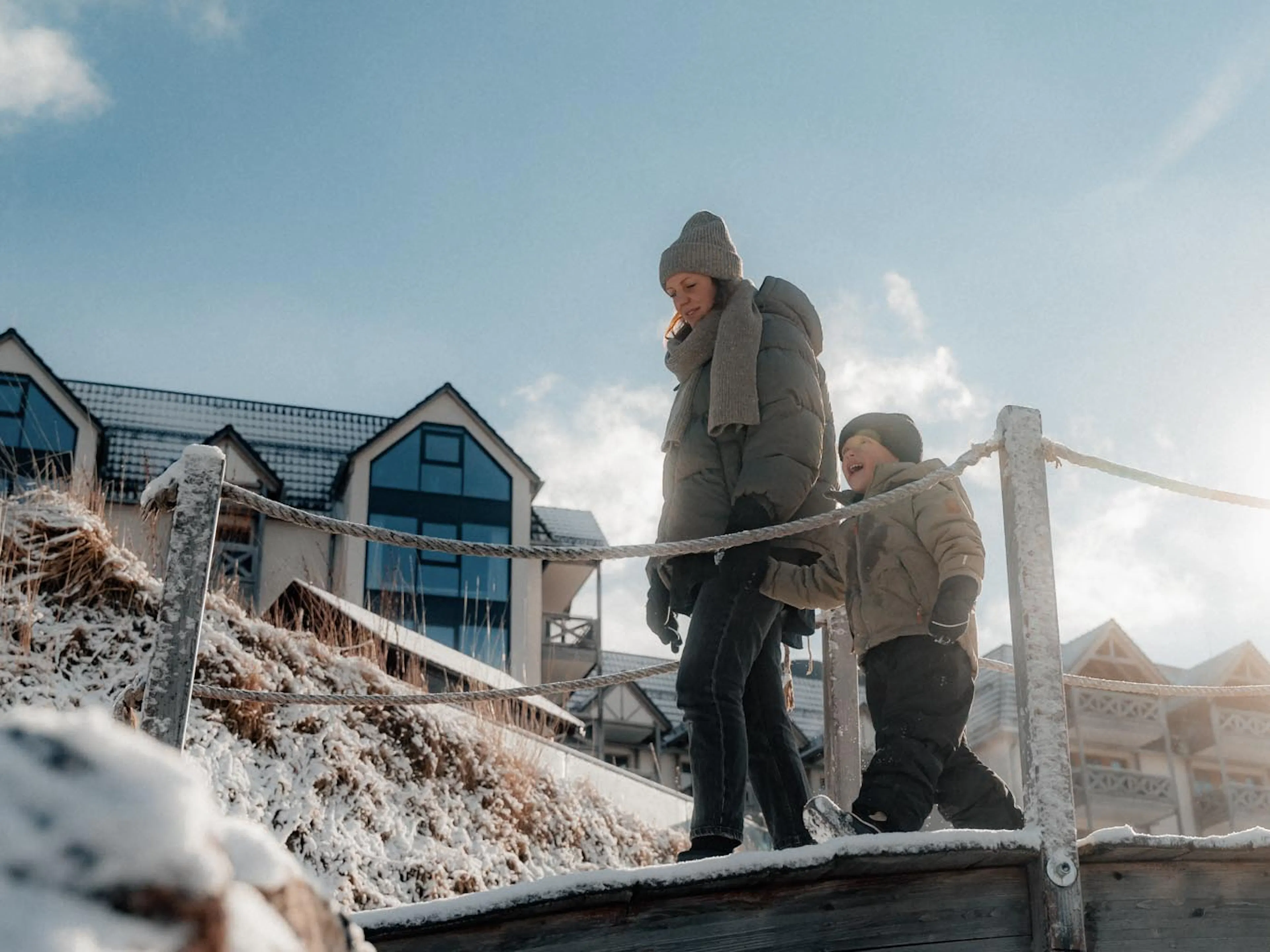 Mama geht mit Kind im Winter im Hotelgarten des The Grand Green - Familux Resorts spazieren.