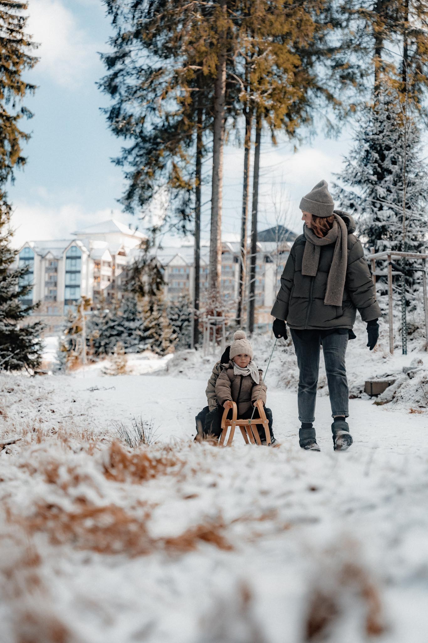 Mother sledging with her children with views of The Grand Green – Familux Resort.