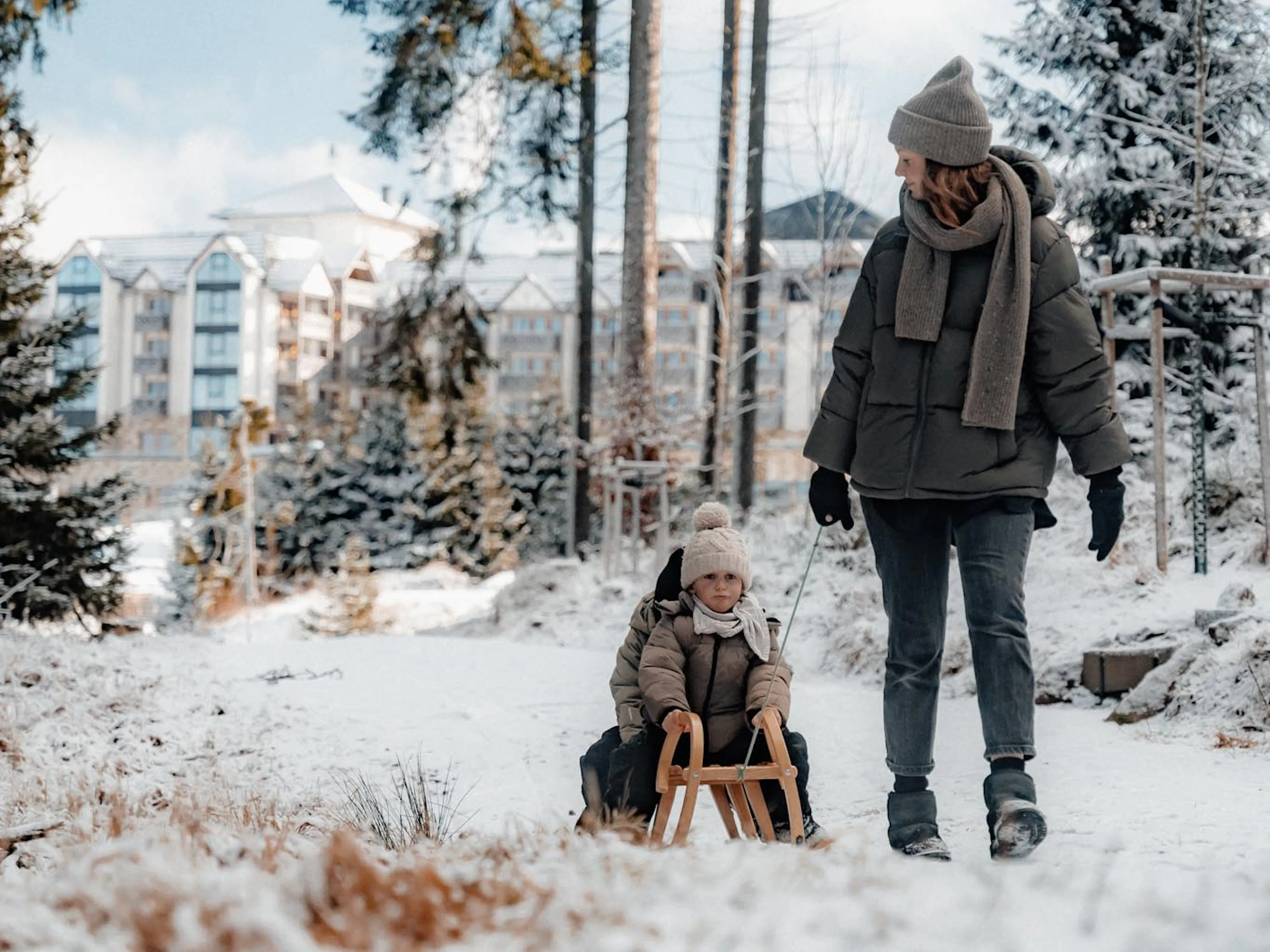 Mother sledging with her children with views of The Grand Green – Familux Resort.