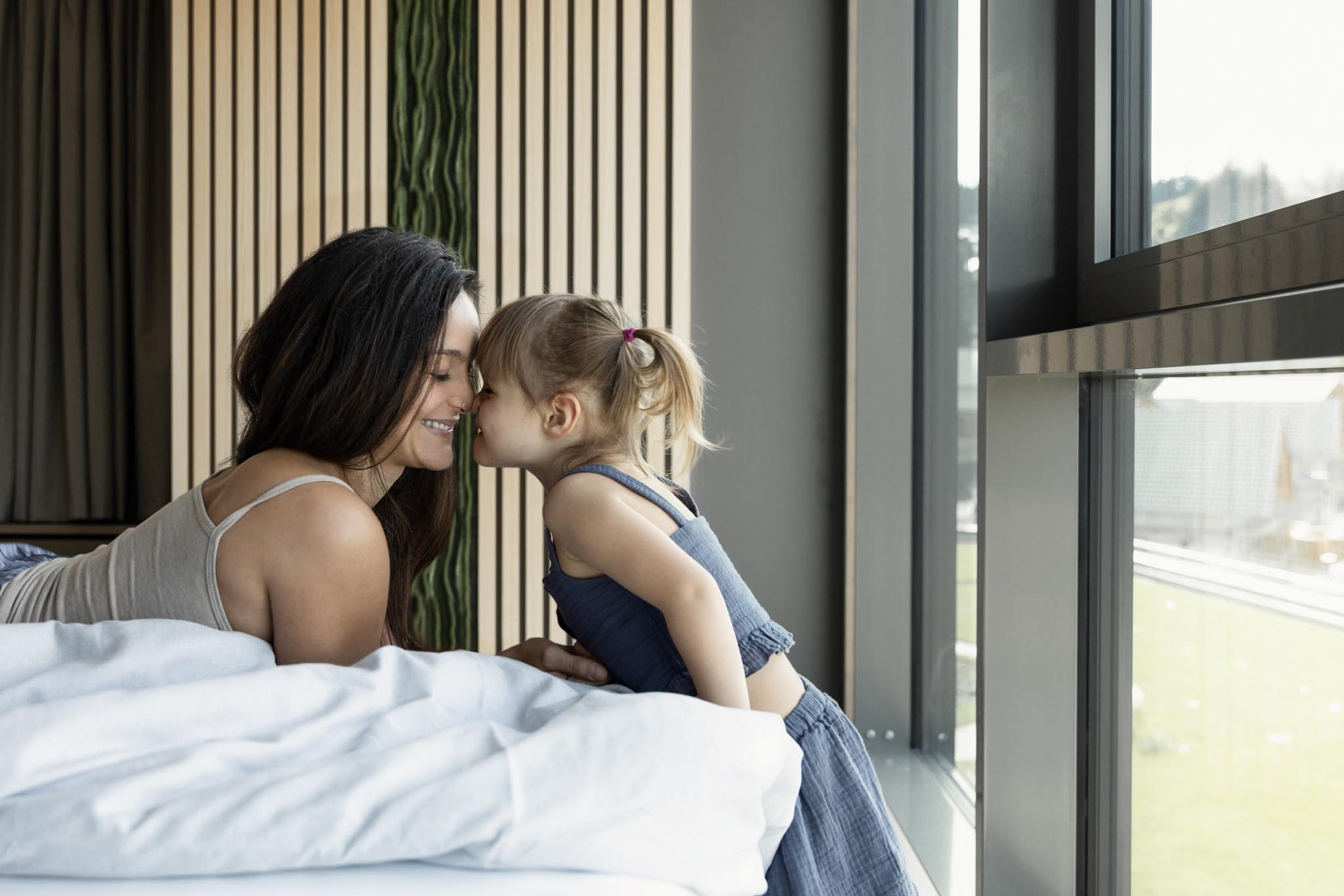 Mama und Tochter kuscheln im Bett einer Familiensuite des The Grand Green - Familux Resorts.