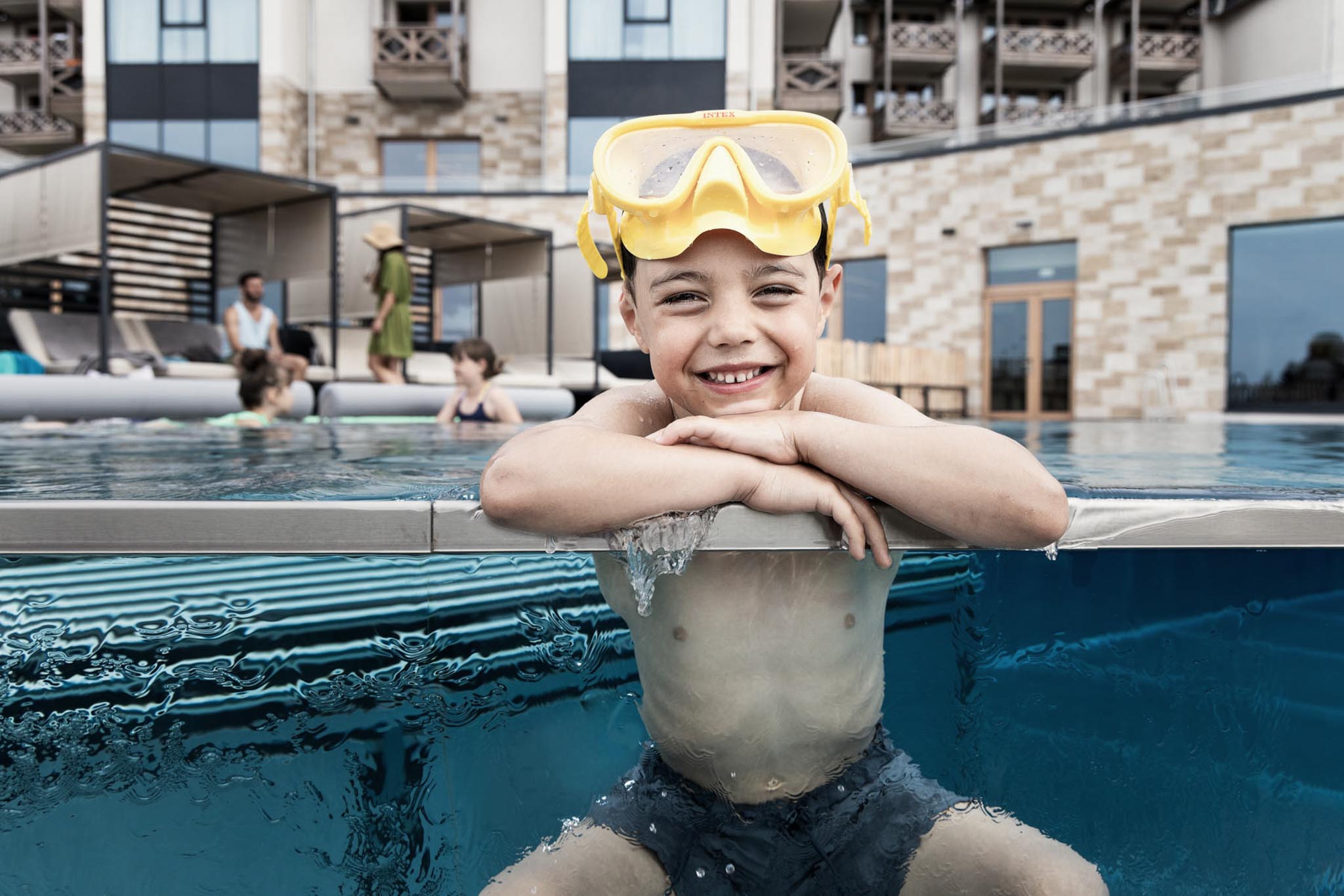 Boy wearing swimming goggles sitting at the poolside at The Grand Green – Familux Resort.