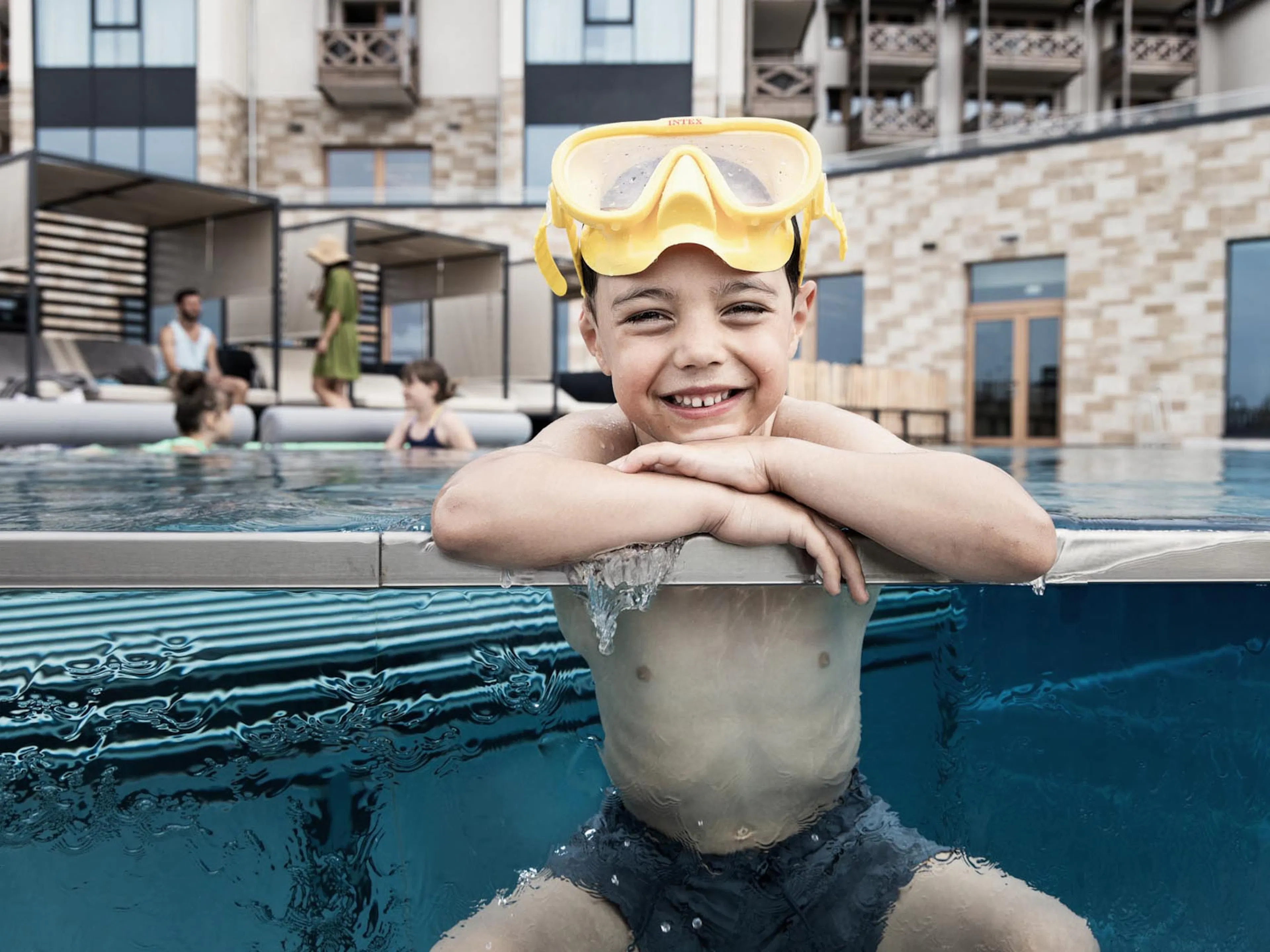 Junge mit Taucherbrille sitzt am Poolrand des The Grand Green - Familux Resorts.