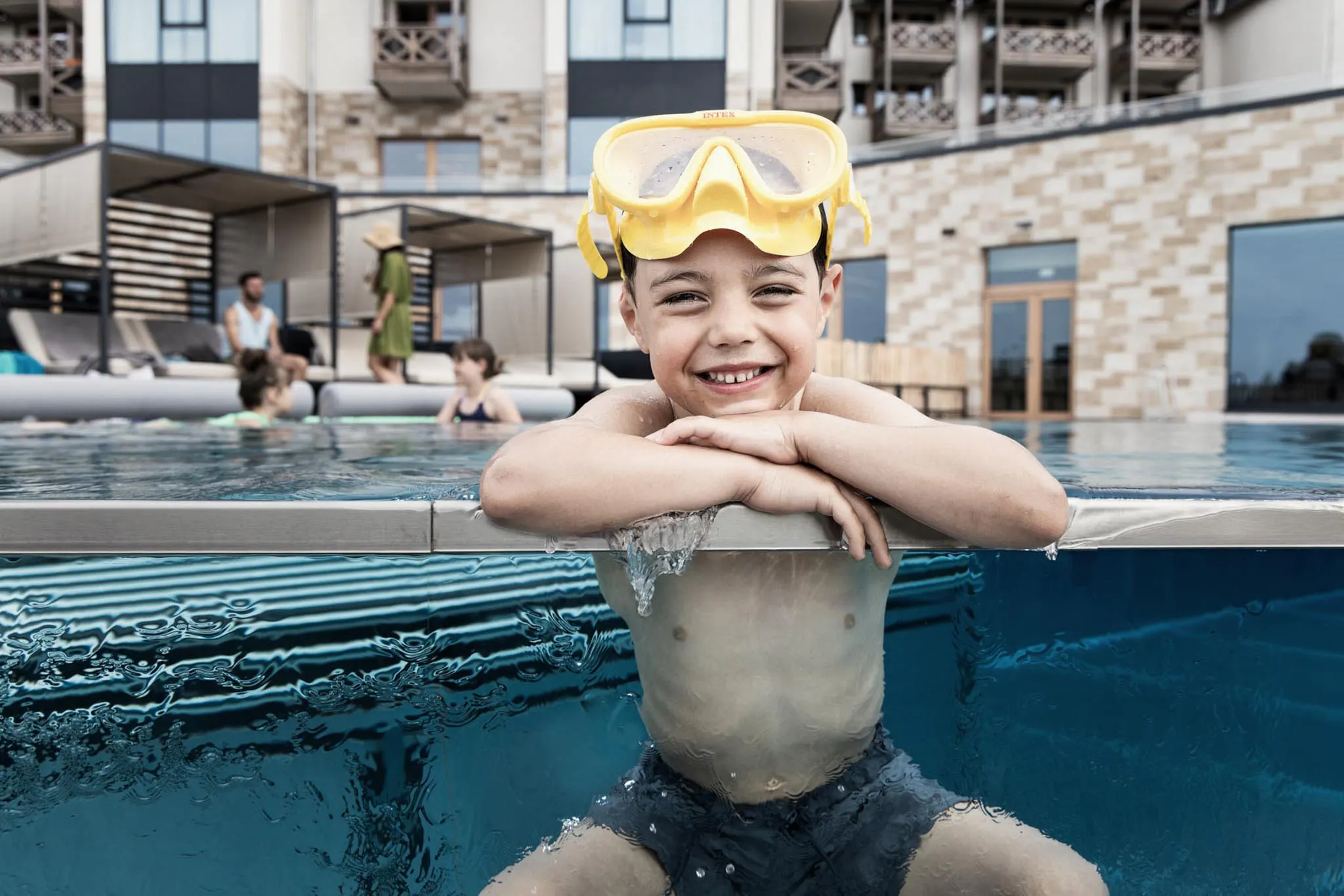 Junge mit Taucherbrille sitzt am Poolrand des The Grand Green - Familux Resorts.