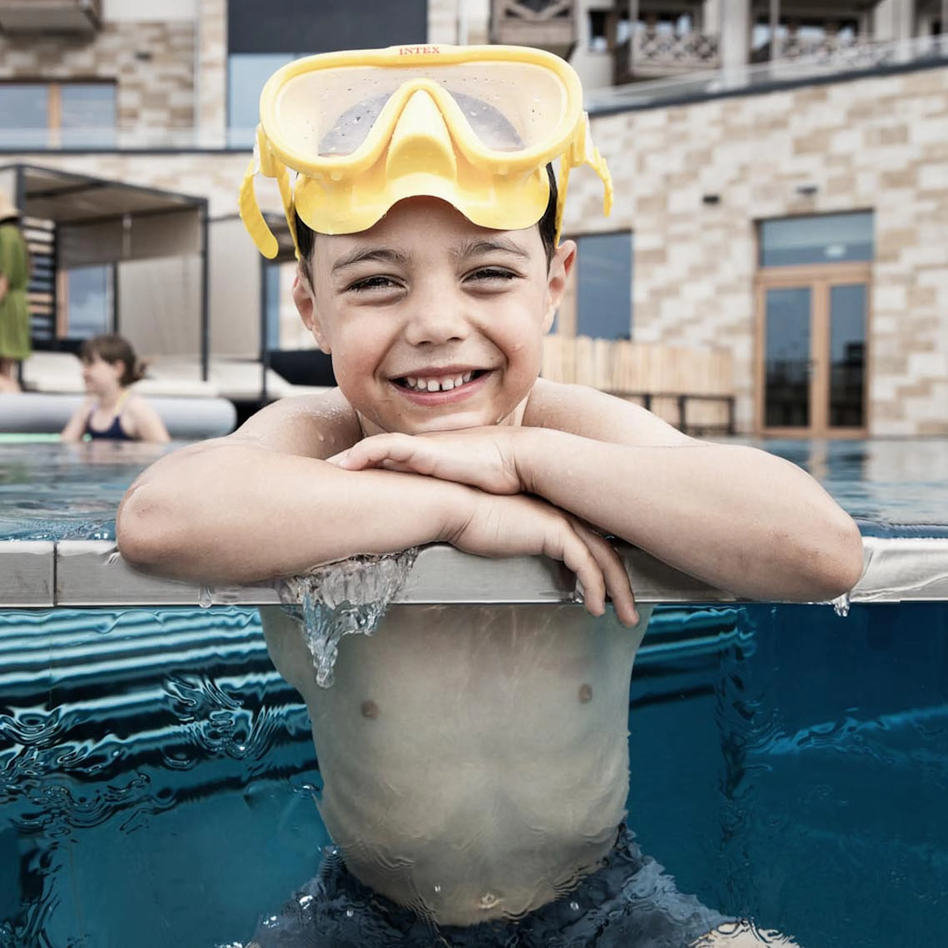 Boy wearing swimming goggles sitting at the poolside at The Grand Green – Familux Resort.
