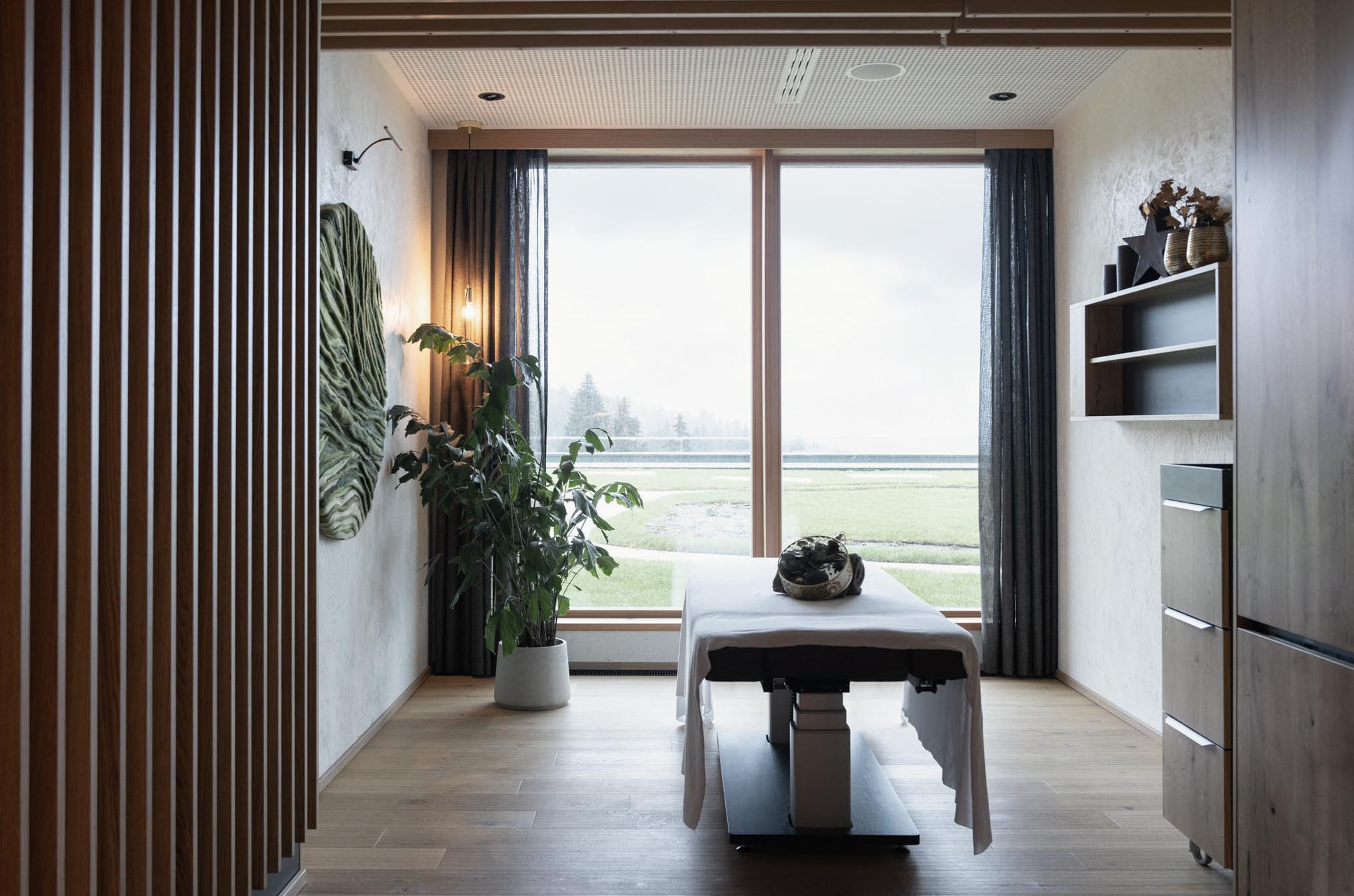 Spa Behandlungsraum mit Massageliege und Aussicht in den Wald im The Grand Green - Familux Resort.