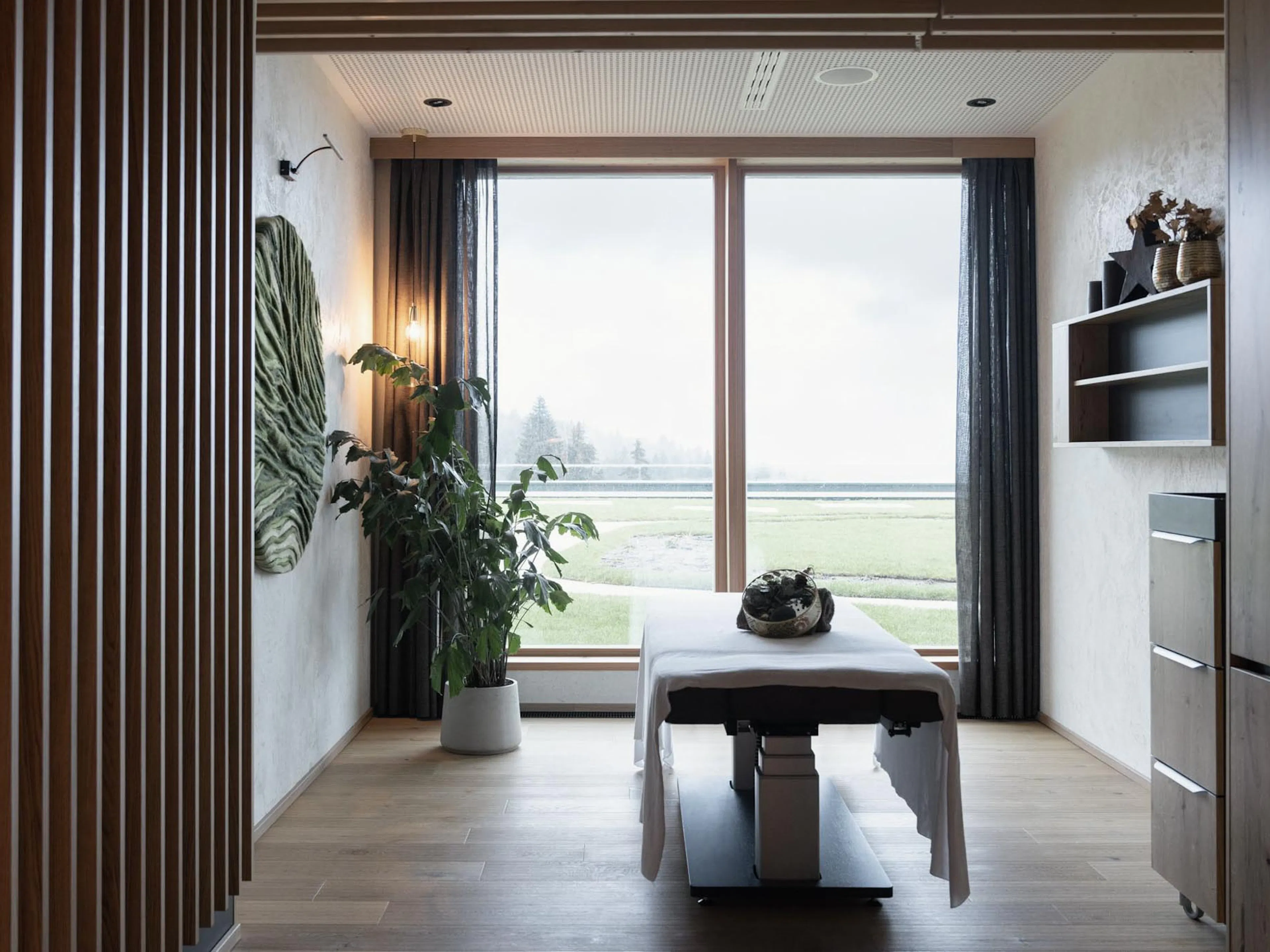 Spa treatment room with massage table and views over the forest at The Grand Green – Familux Resort.