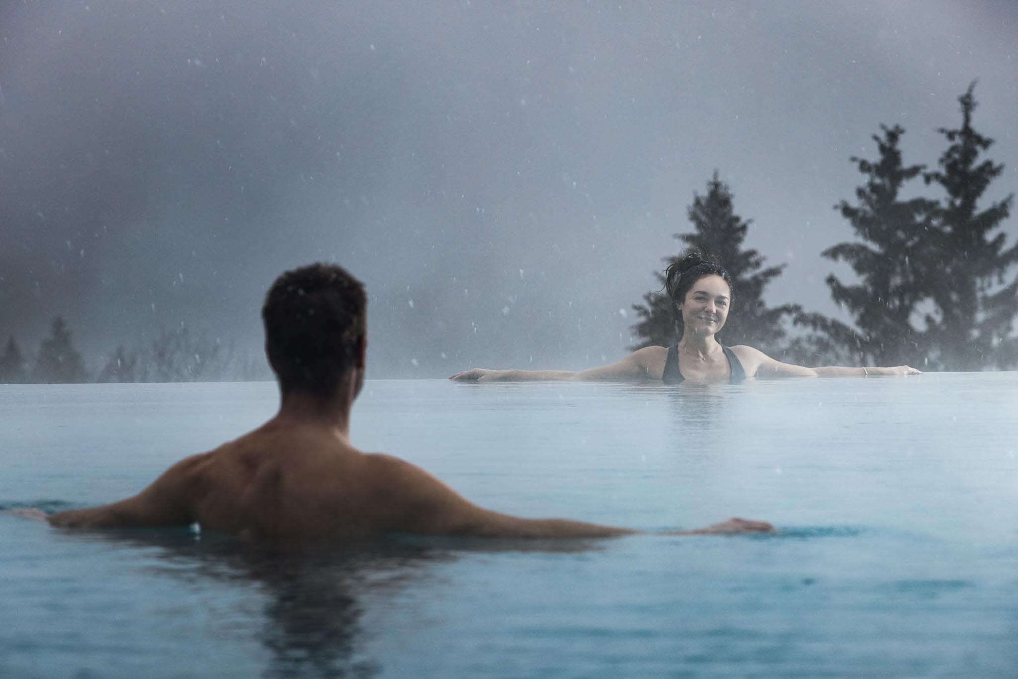 Man and woman swimming in the outdoor pool overlooking the forest at The Grand Green – Familux Resort.