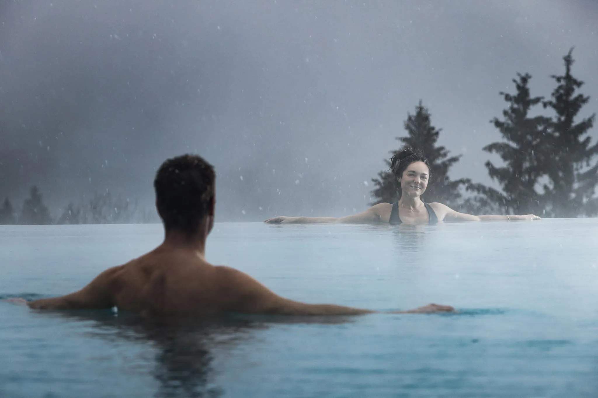 Mann und Frau schwimmen im Outdoor Pool mit Blick über den Wald im The Grand Green - Familux Resort.