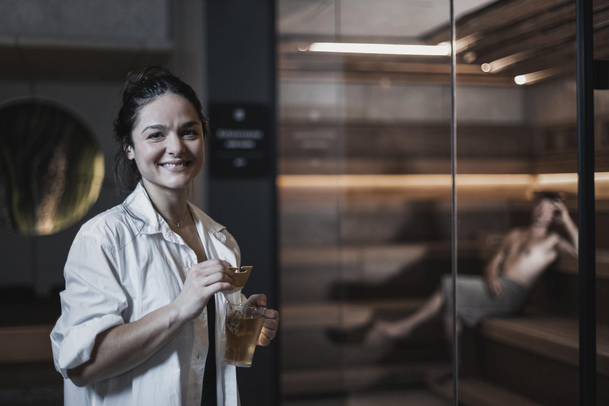 Woman standing with tea in front of the sauna in the wellness area of The Grand Green – Familux Resort.