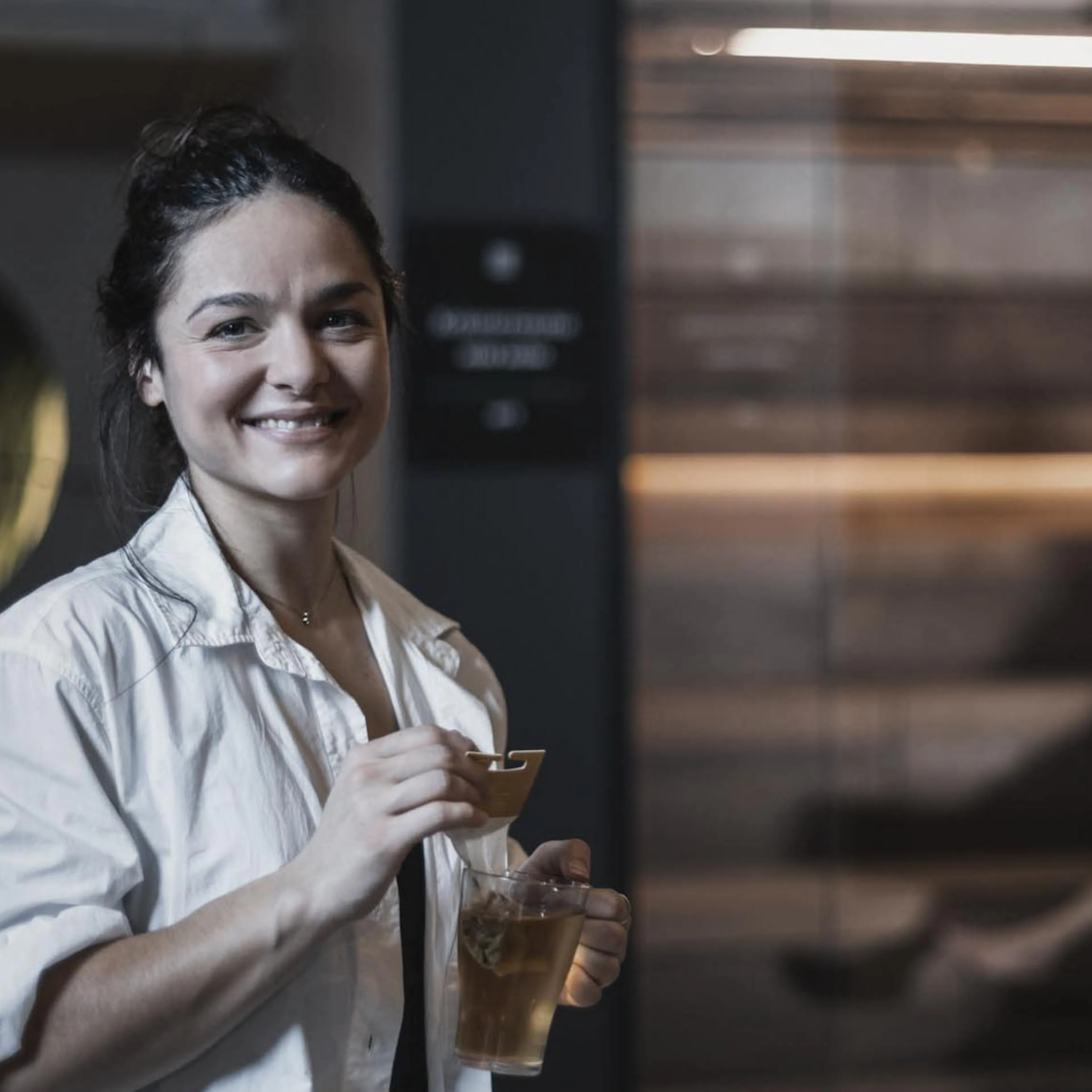 Frau steht mit Tee vor der Sauna im Wellnessbereich des The Grand Green - Familux Resorts.