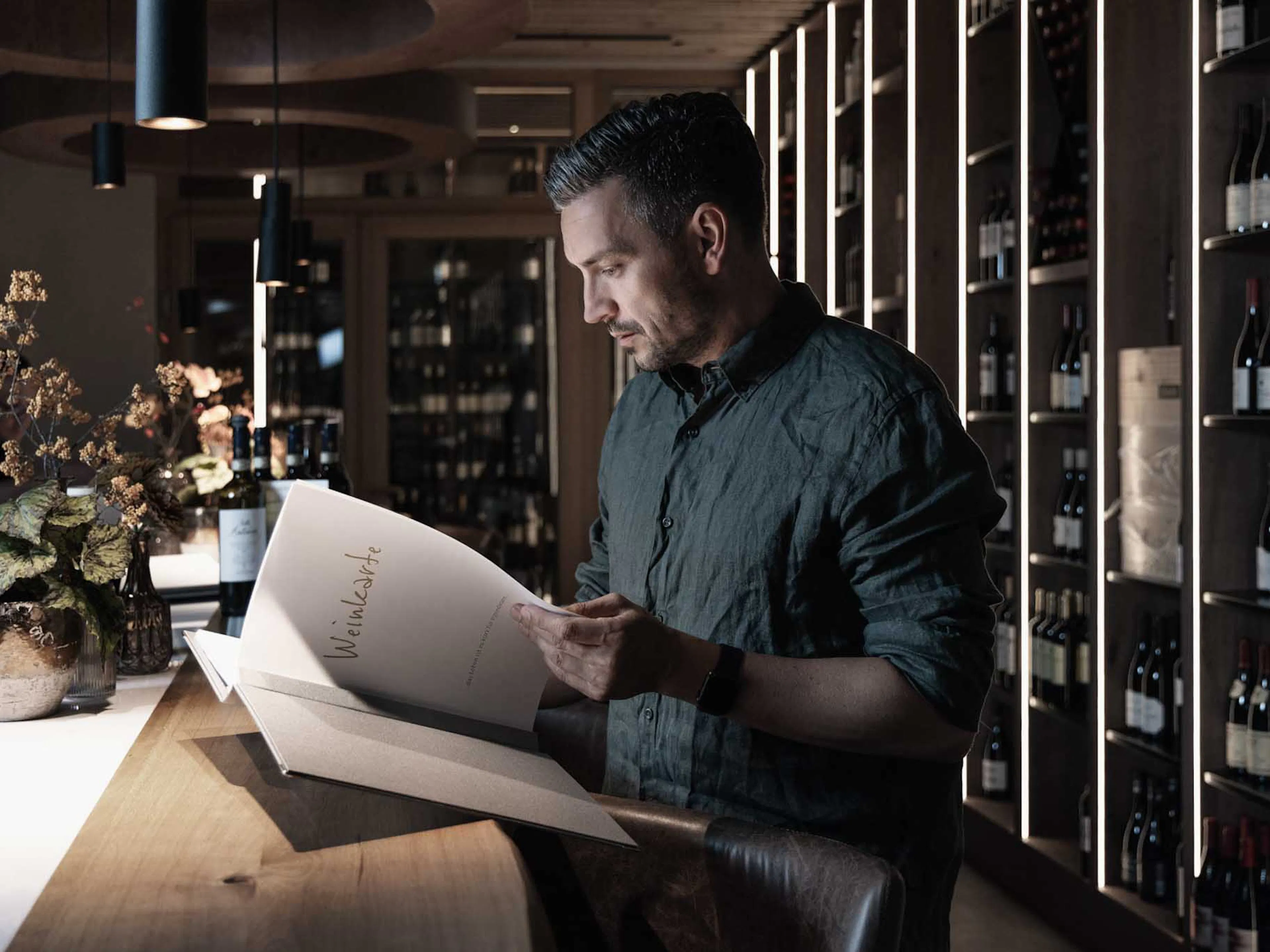 Man standing in the wine cellar of The Grand Green – Familux Resort reading a wine menu.