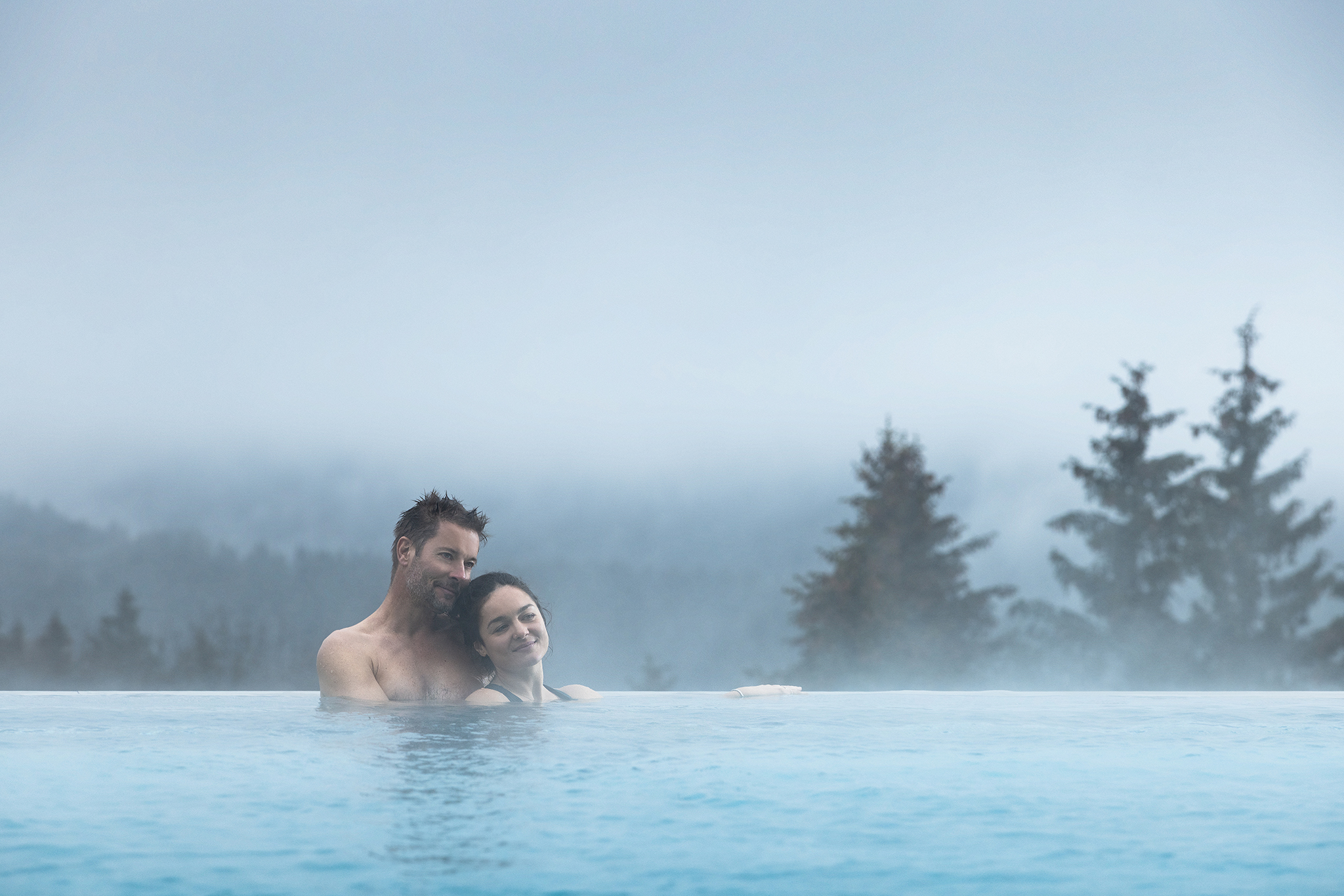 Mann und Frau schwimmen im Outdoor Pool mit Blick über den Wald im The Grand Green - Familux Resort.
