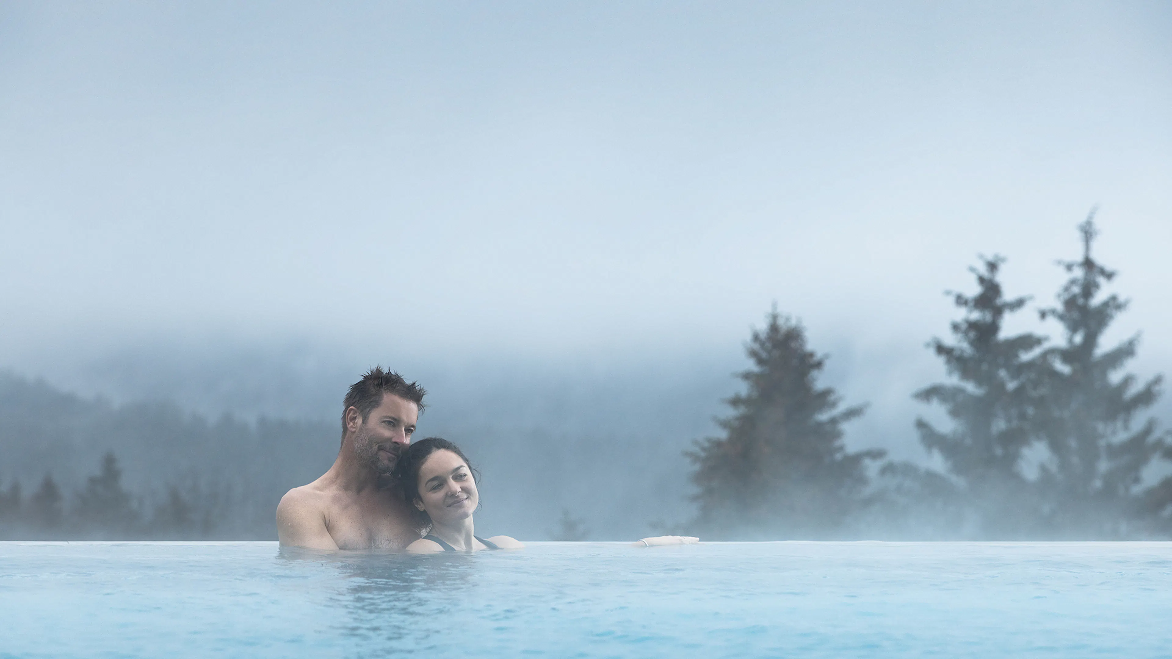Mann und Frau schwimmen im Outdoor Pool mit Blick über den Wald im The Grand Green - Familux Resort.