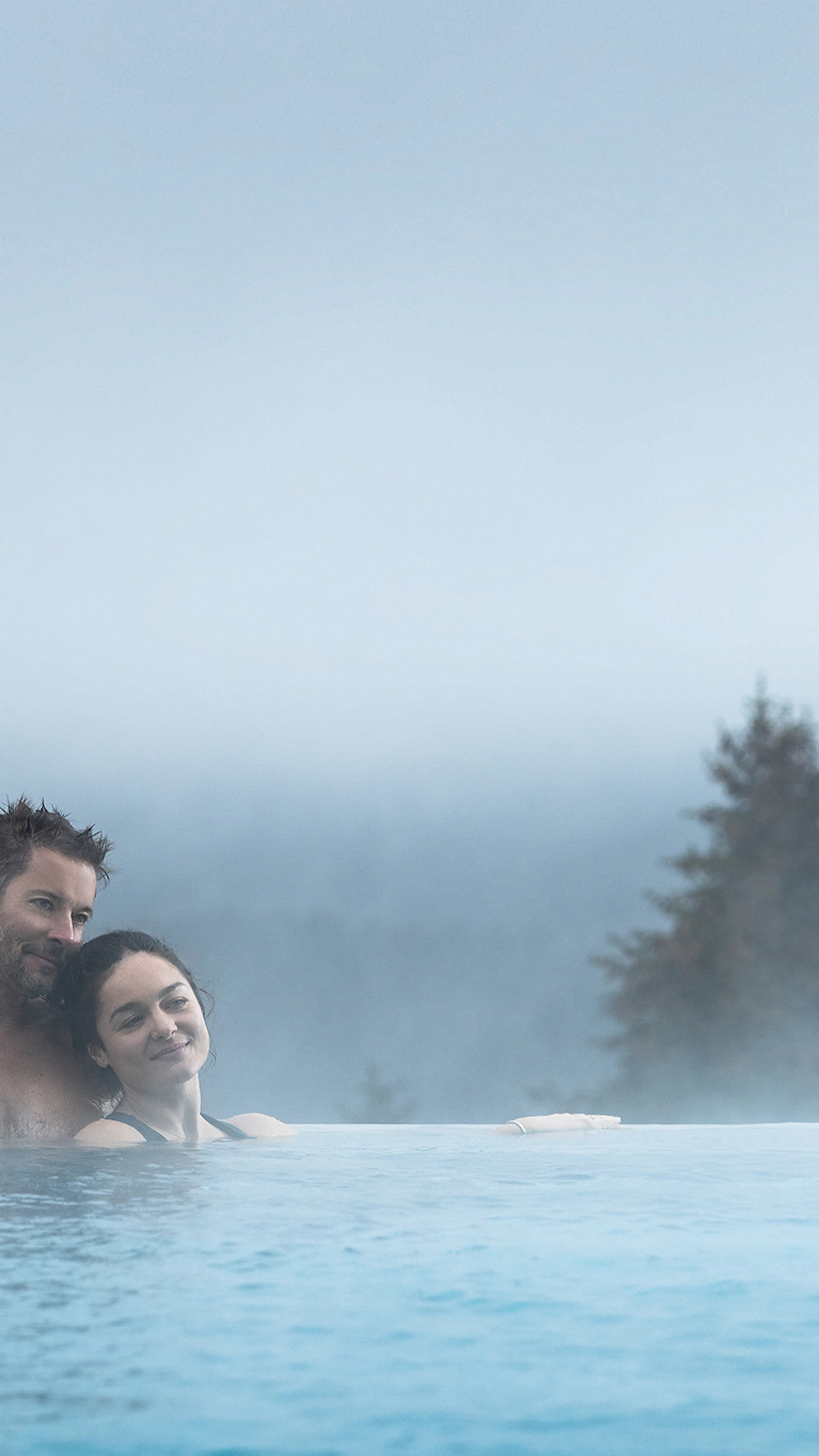 Mann und Frau schwimmen im Outdoor Pool mit Blick über den Wald im The Grand Green - Familux Resort.