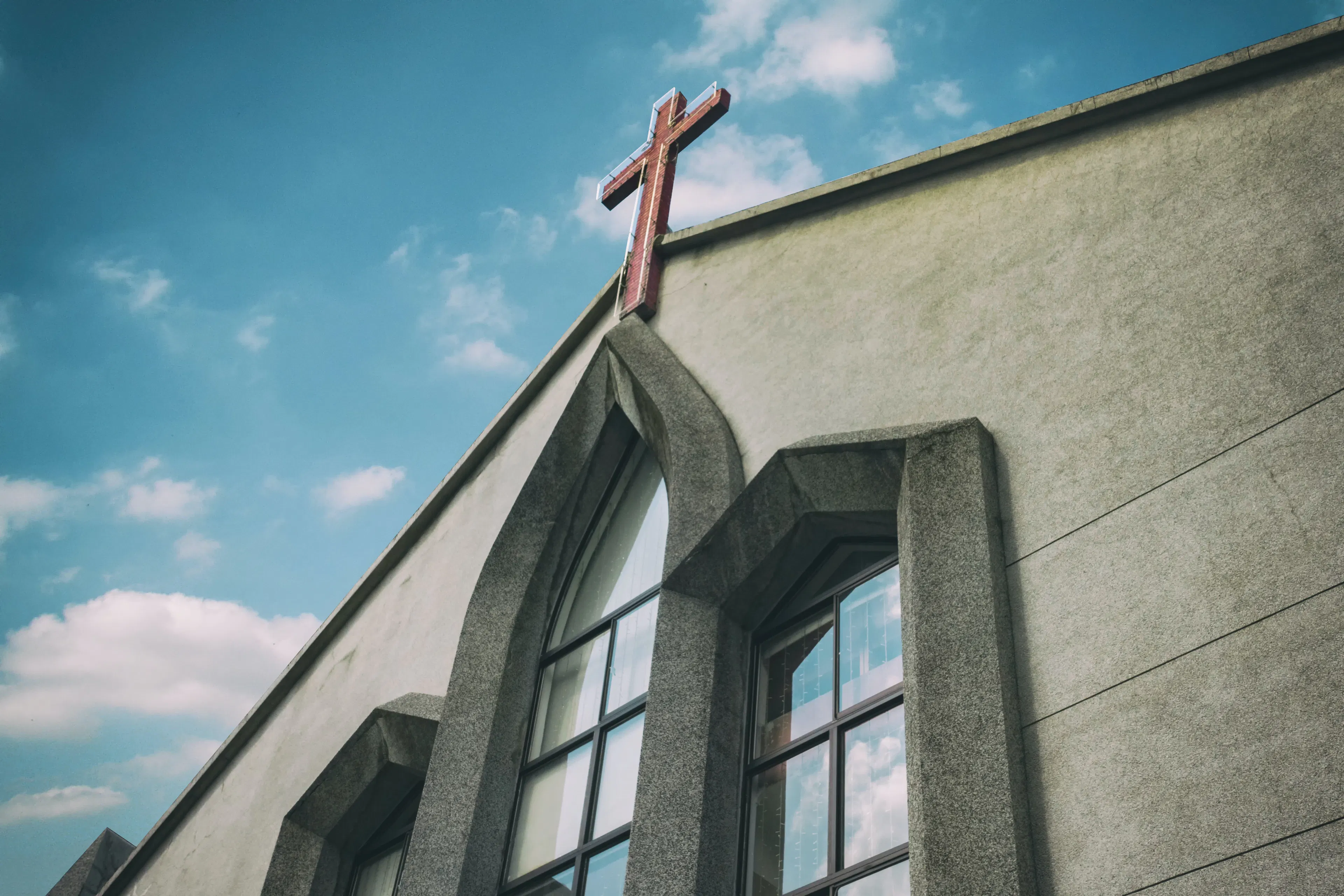 A neon cross in daylight on top of a church building.