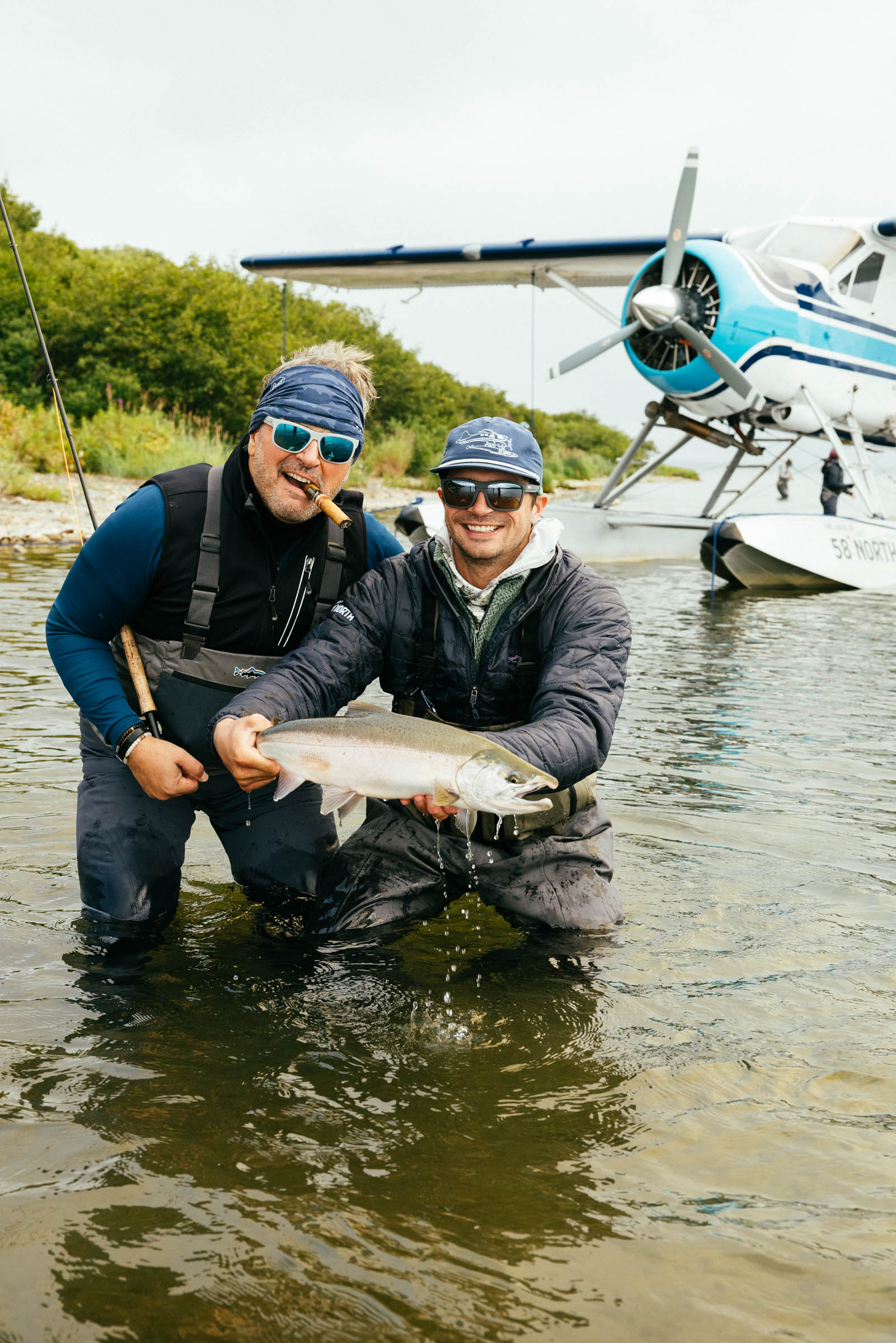 Two anglers holding a trophy fish in shallow water with an Alaska floatplane behind them on a guided fly-fishing trip