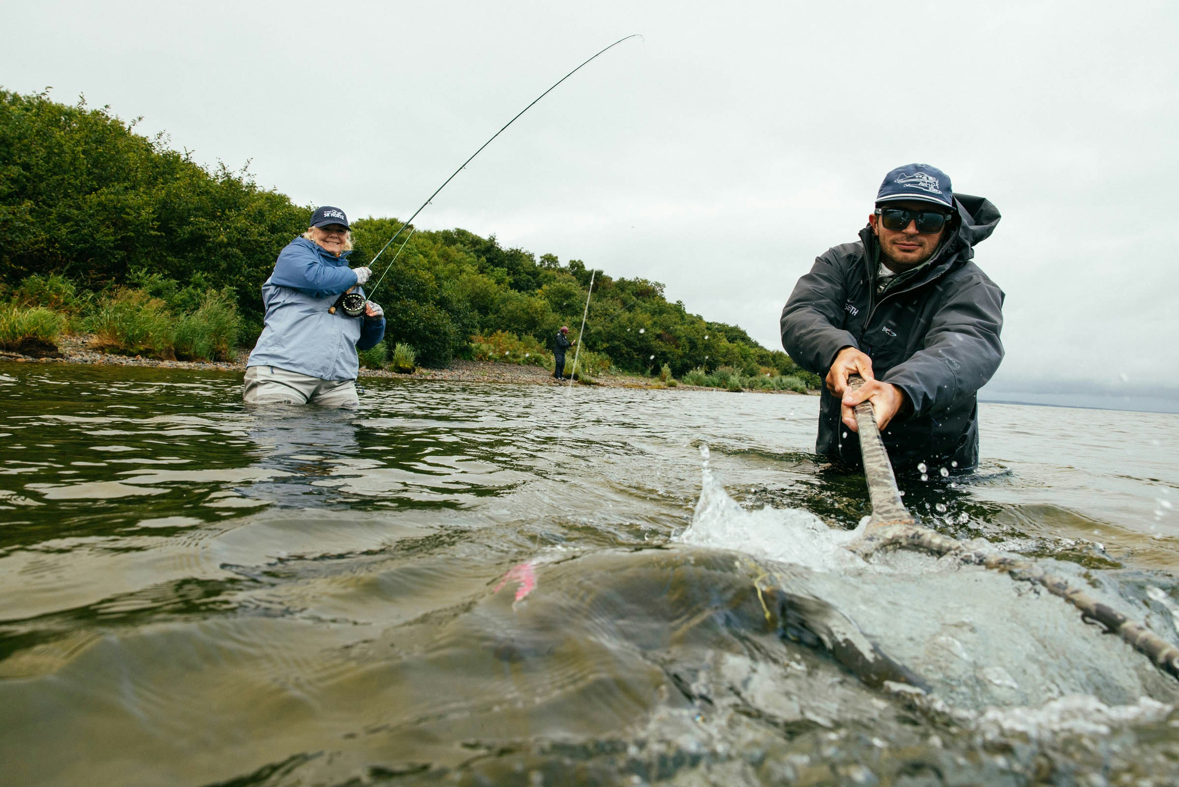 Angler fighting and landing a large fish in Alaskan waters with the guide assisting with a net