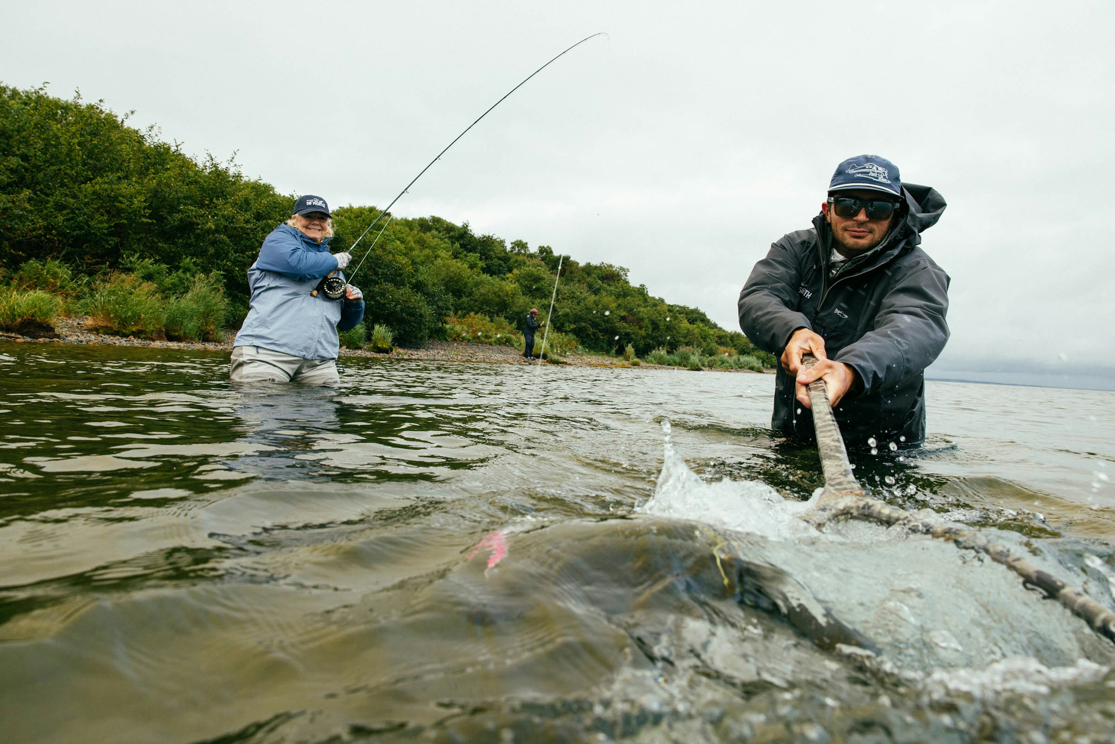Angler fighting and landing a large fish in Alaskan waters with the guide assisting with a net