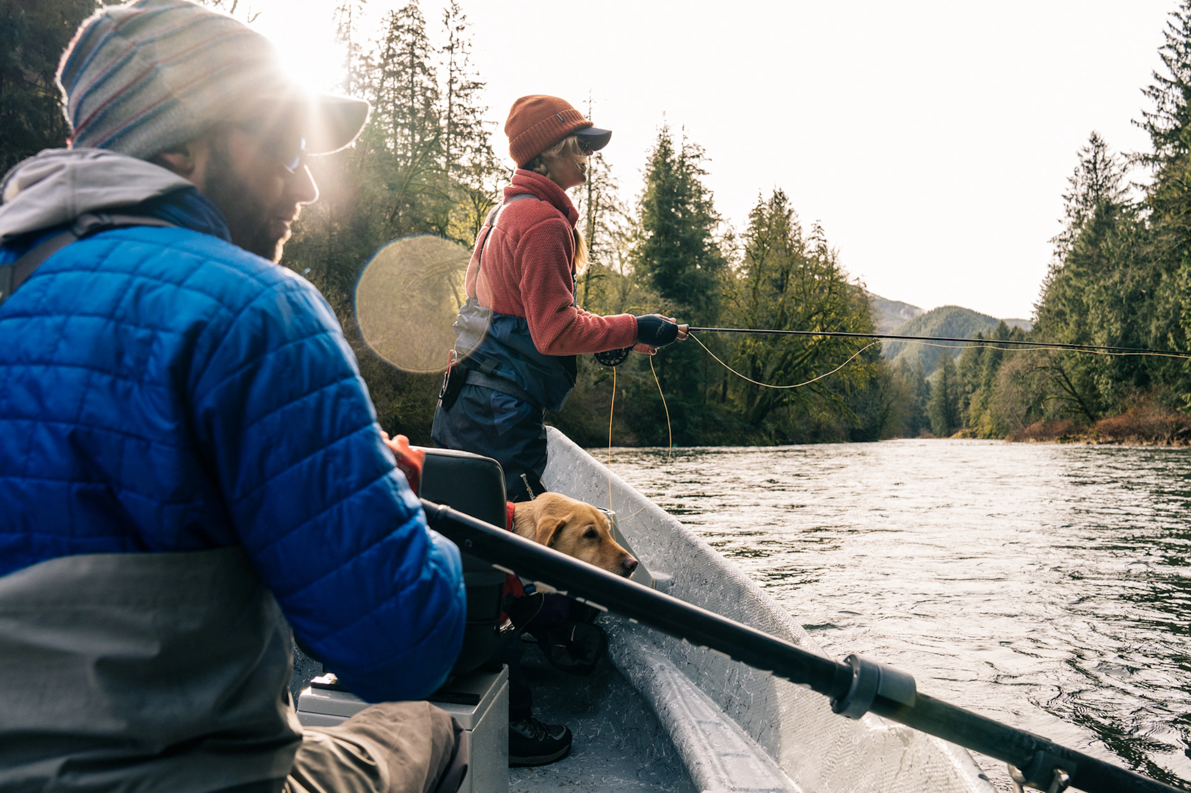 Anglers fly fishing from a drift boat on a forested Oregon Coast river with a dog on board