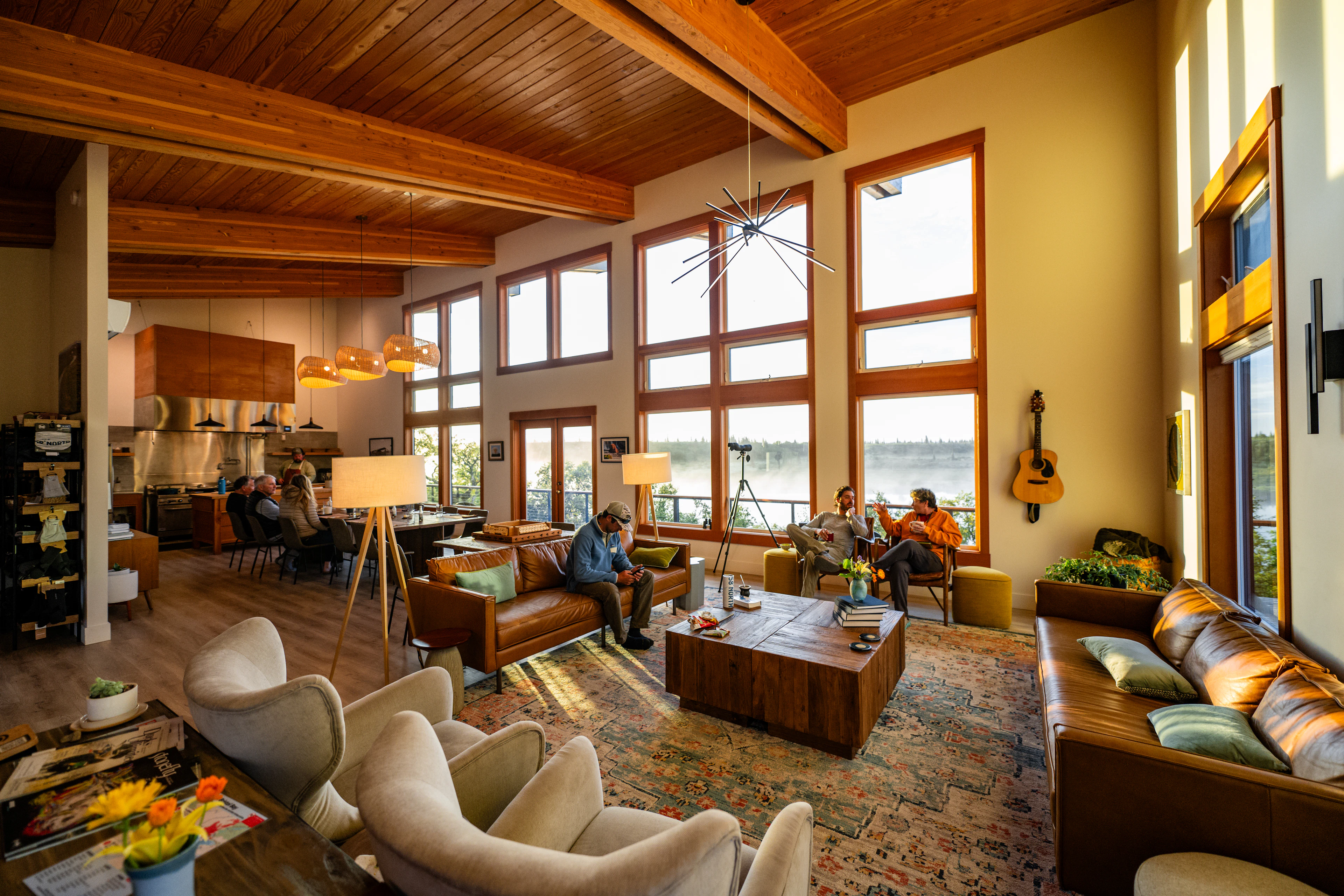 Guests relax inside the main lodge at The Lodge at 58* North, a luxury fishing lodge in Bristol Bay, Alaska, with river views and warm natural light.