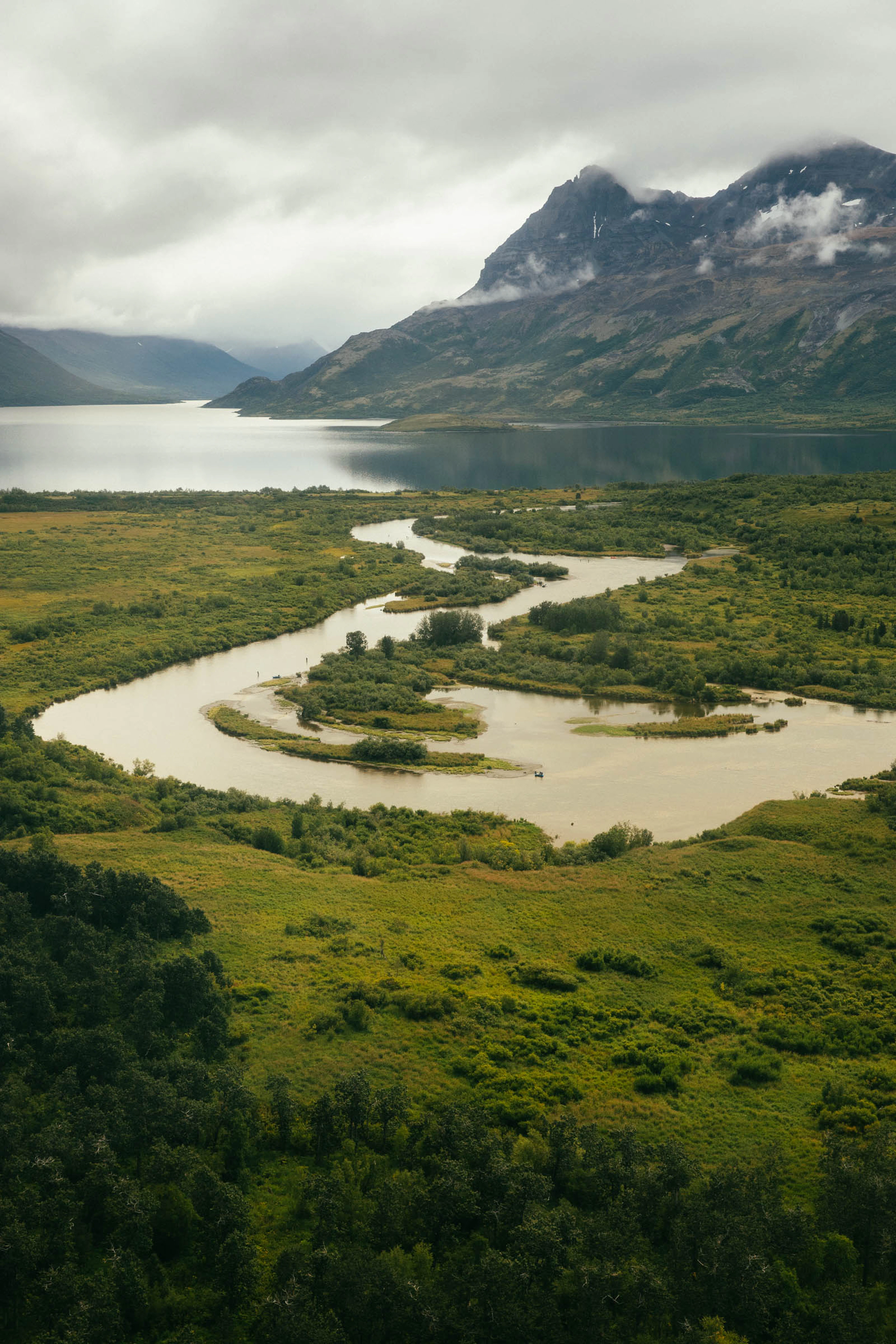 Aerial view of a winding river flowing toward a mountain lake in remote Alaska near The Lodge at 58* North