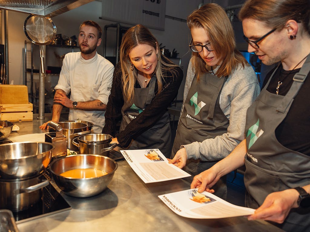 Vier NextGenners kijken geïnteresseerd naar een recept tijdens het The.NextGen kook evenement.