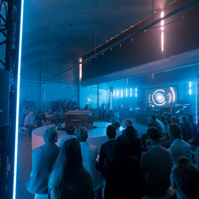 Donkere ruimte met blauw licht en publiek tijdens community event.