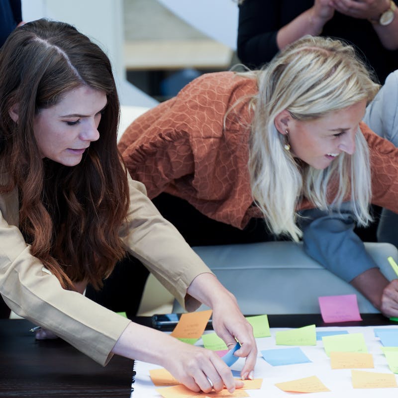 2 dames die hun ideeën schrijven op sticky notes gedurende community event.