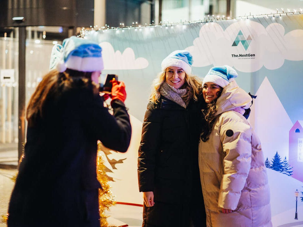 Twee The.NextGen medewerkers poseren voor derde medewerker die een foto maakt met een polaroid camera.